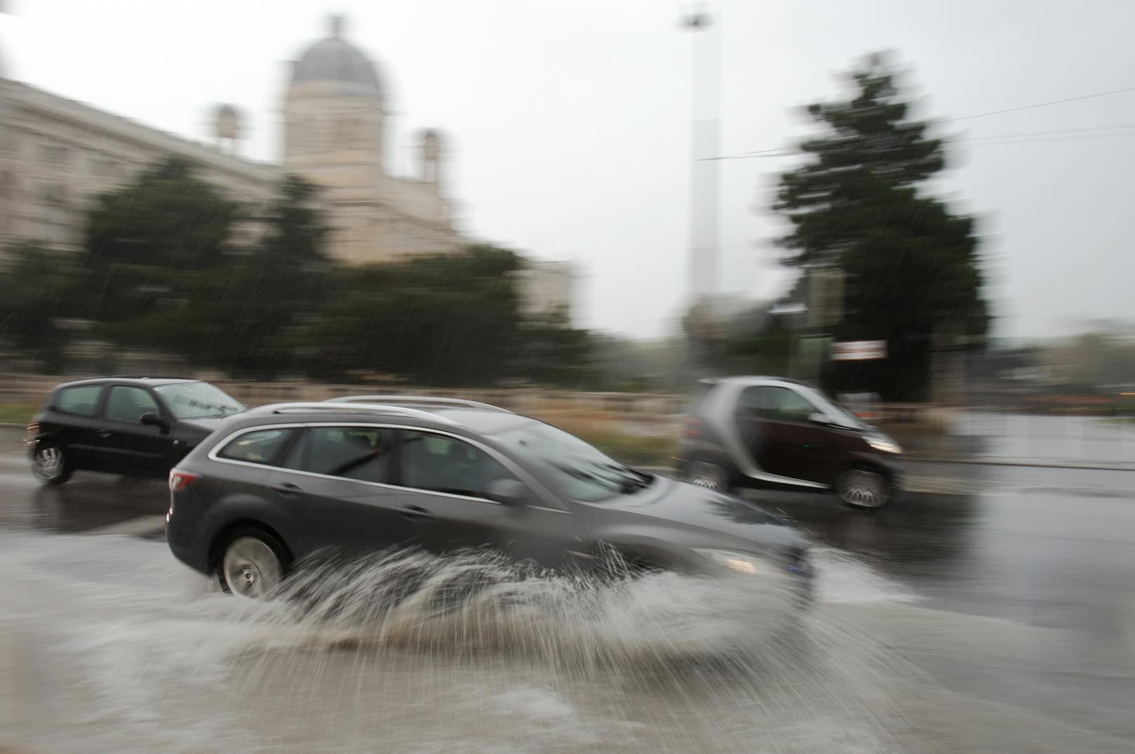 Symbolbild. Fahrzeuge verursachen Wasserfontänen während des fahrens über eine überflutete Straße am Museumsplatz in Wien am 25. September 2020.