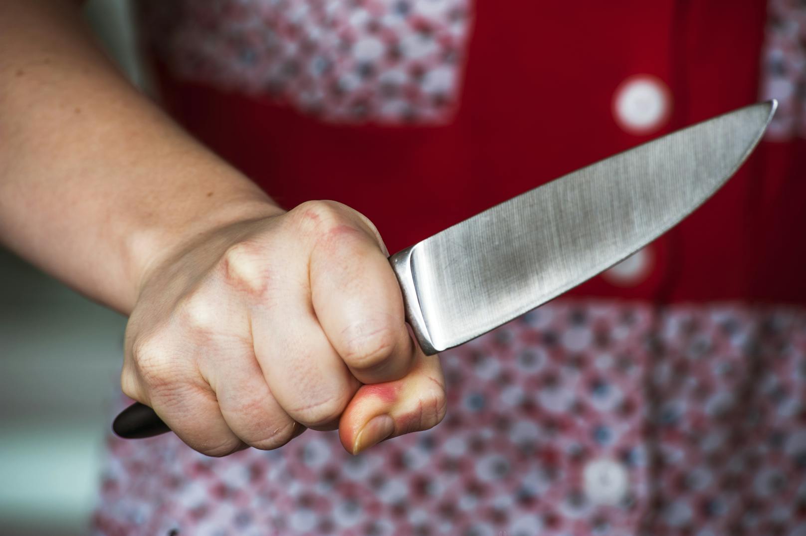 Eine Frau hält verkrampft ein Küchenmesser vor sich. (Symbolfoto)