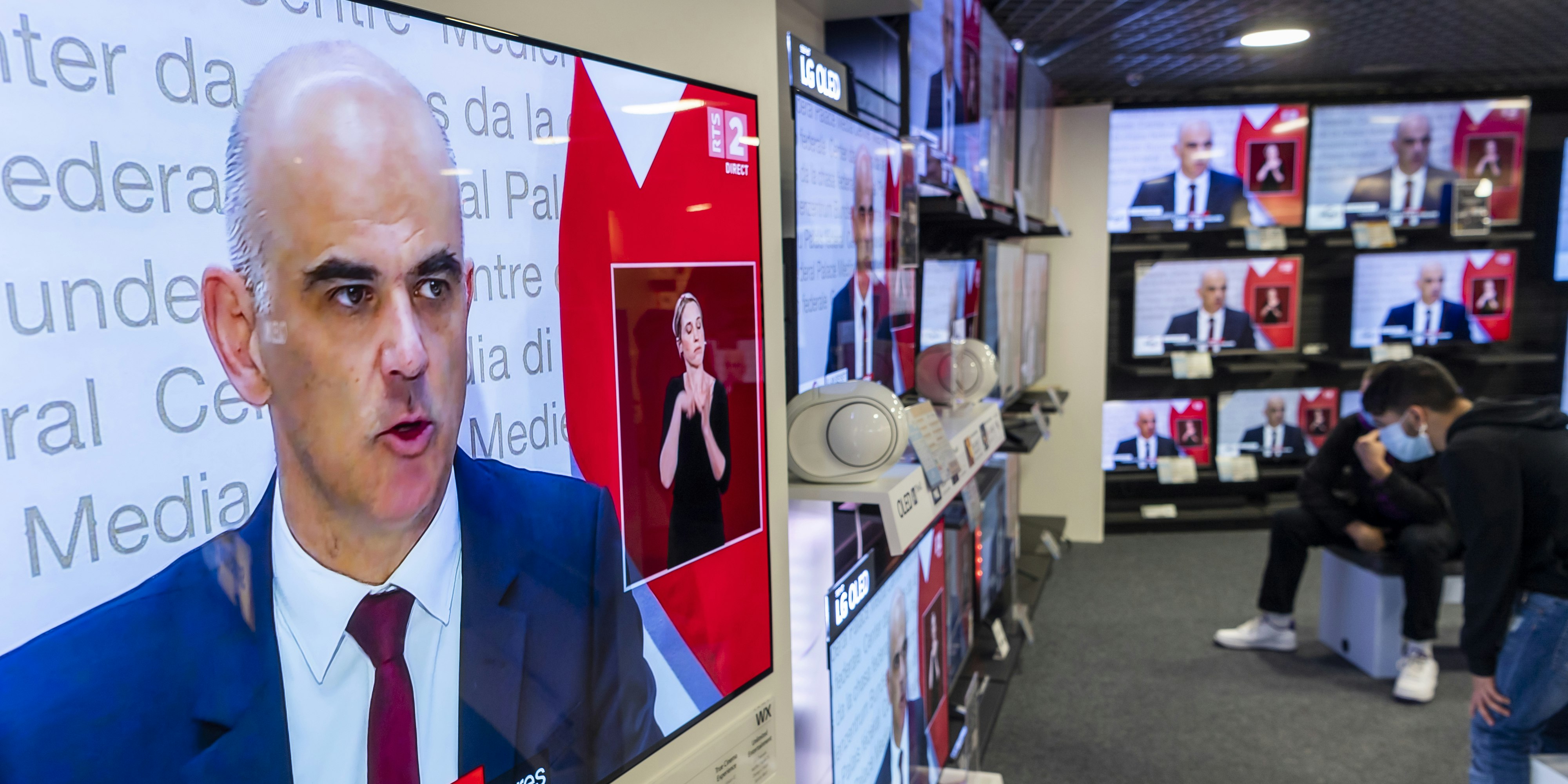 Menschen in Schutzmasken lauschen der Pressekonferenz von Gesundheitsminister Alain Berset: die Schweiz verschärft ihre Coronamaßnahmen