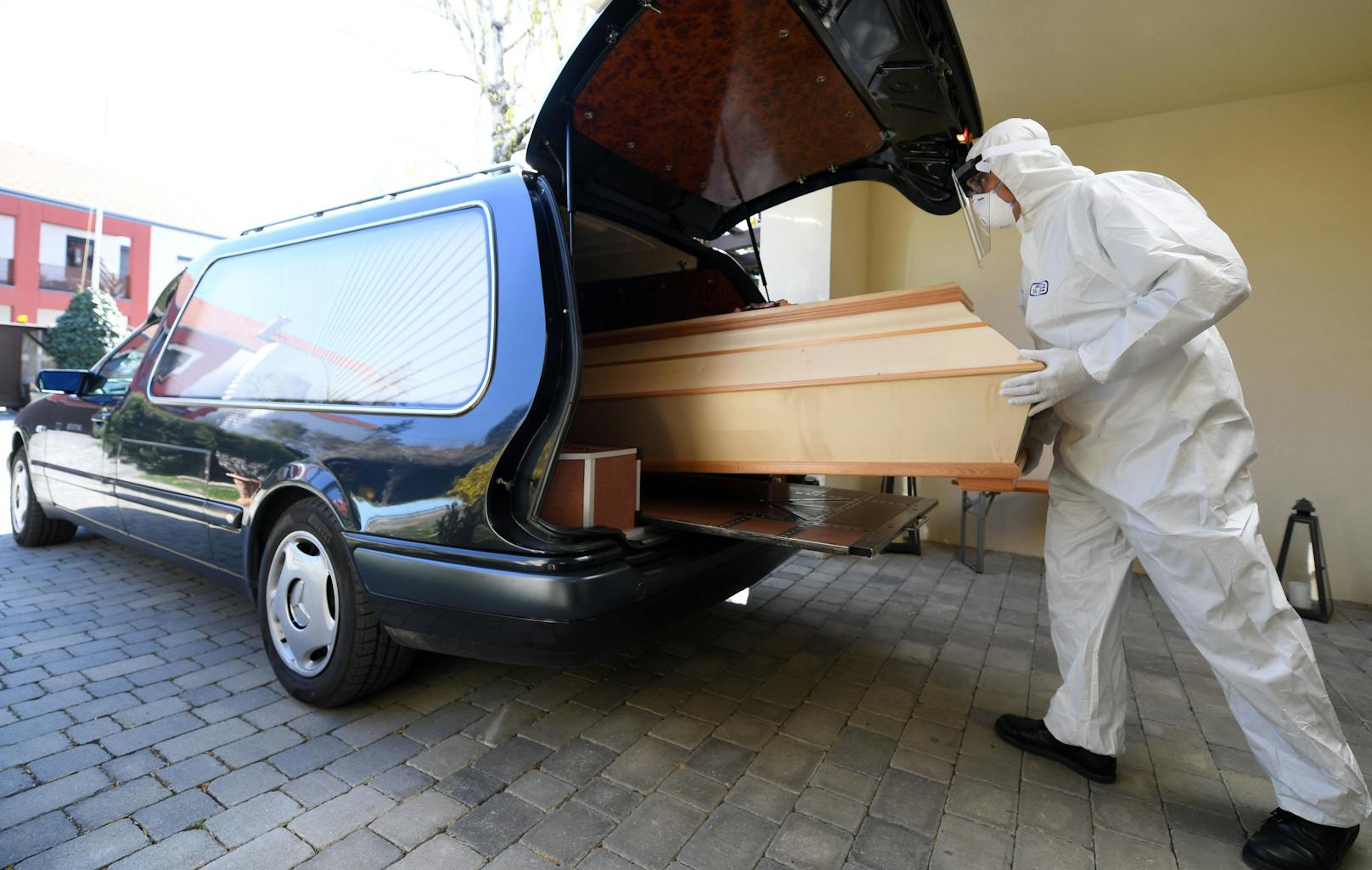 Ein Bestatter in Schutzkleidung schiebt einen Sarg in einen Leichenwagen (Symbolbild).