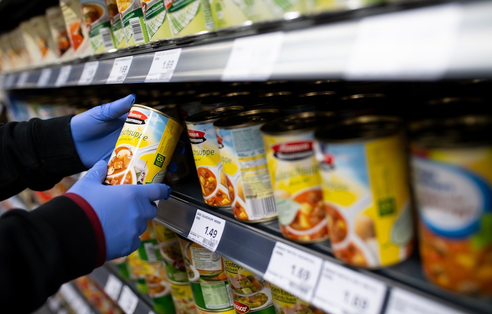 Eine Supermarkt-Angestellte füllt Regale mit Dosensuppe auf.