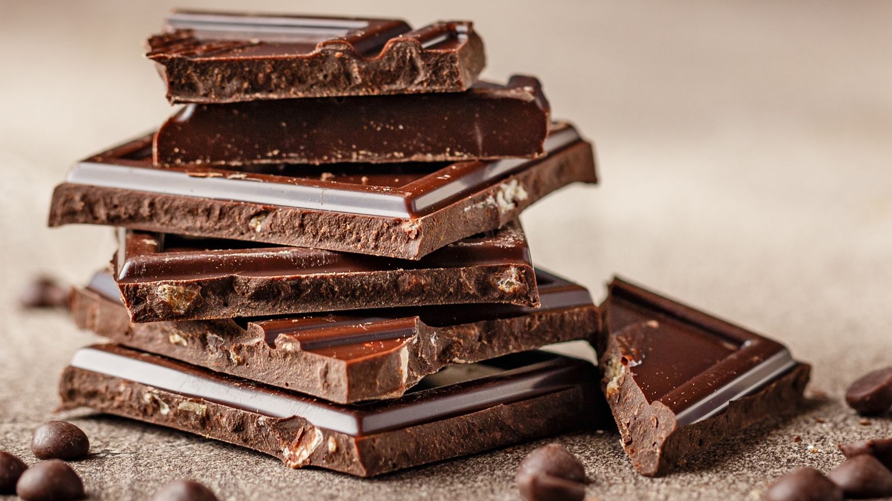 Slices of dark chocolate with chocolate chips on brown background close-up. Long wide banner