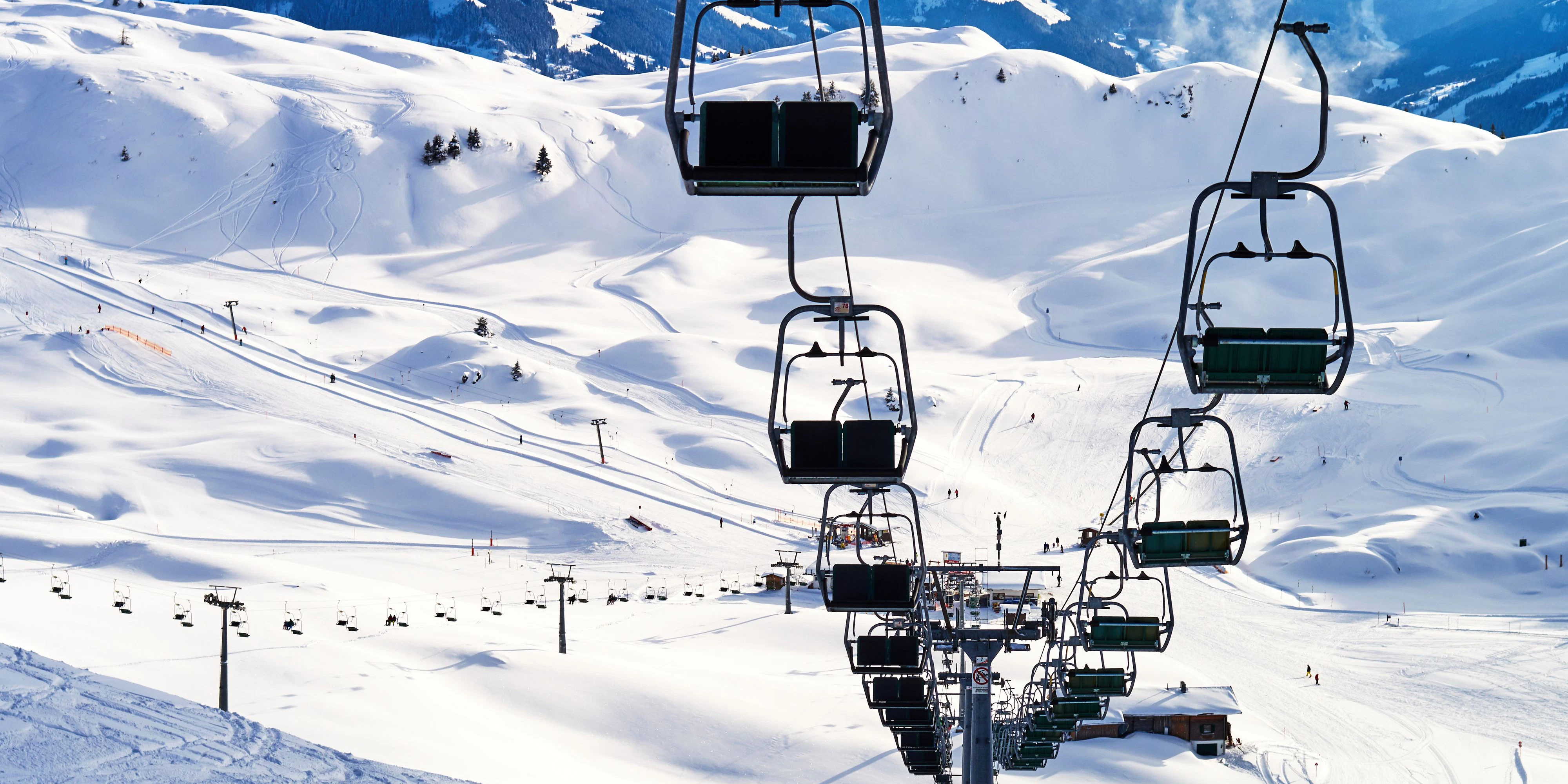 a large ski chair lift above a steep ski slope dotted with tracks on the snowy top of a high mountain in the Austrian Alps and a small chalet