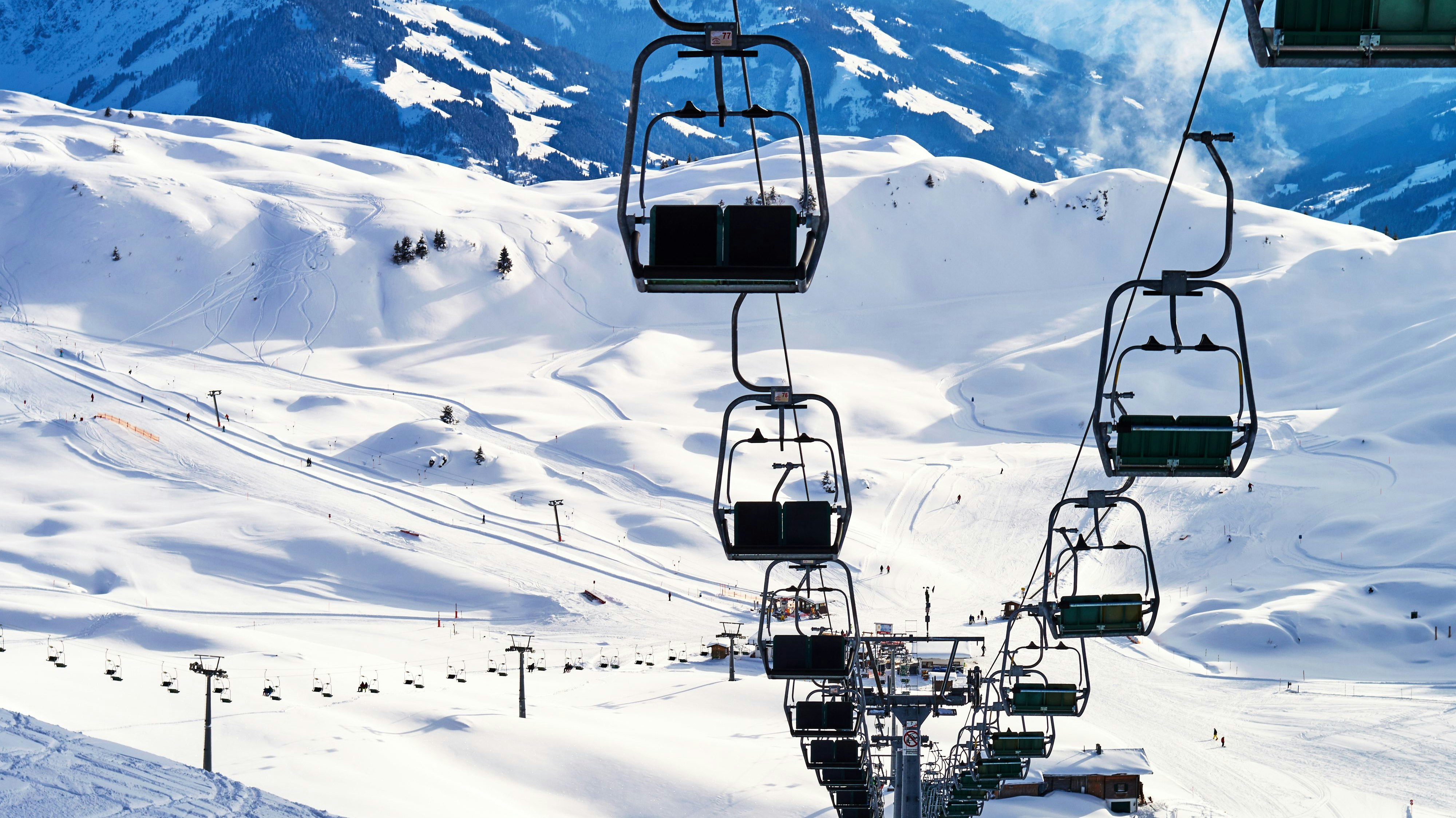 a large ski chair lift above a steep ski slope dotted with tracks on the snowy top of a high mountain in the Austrian Alps and a small chalet