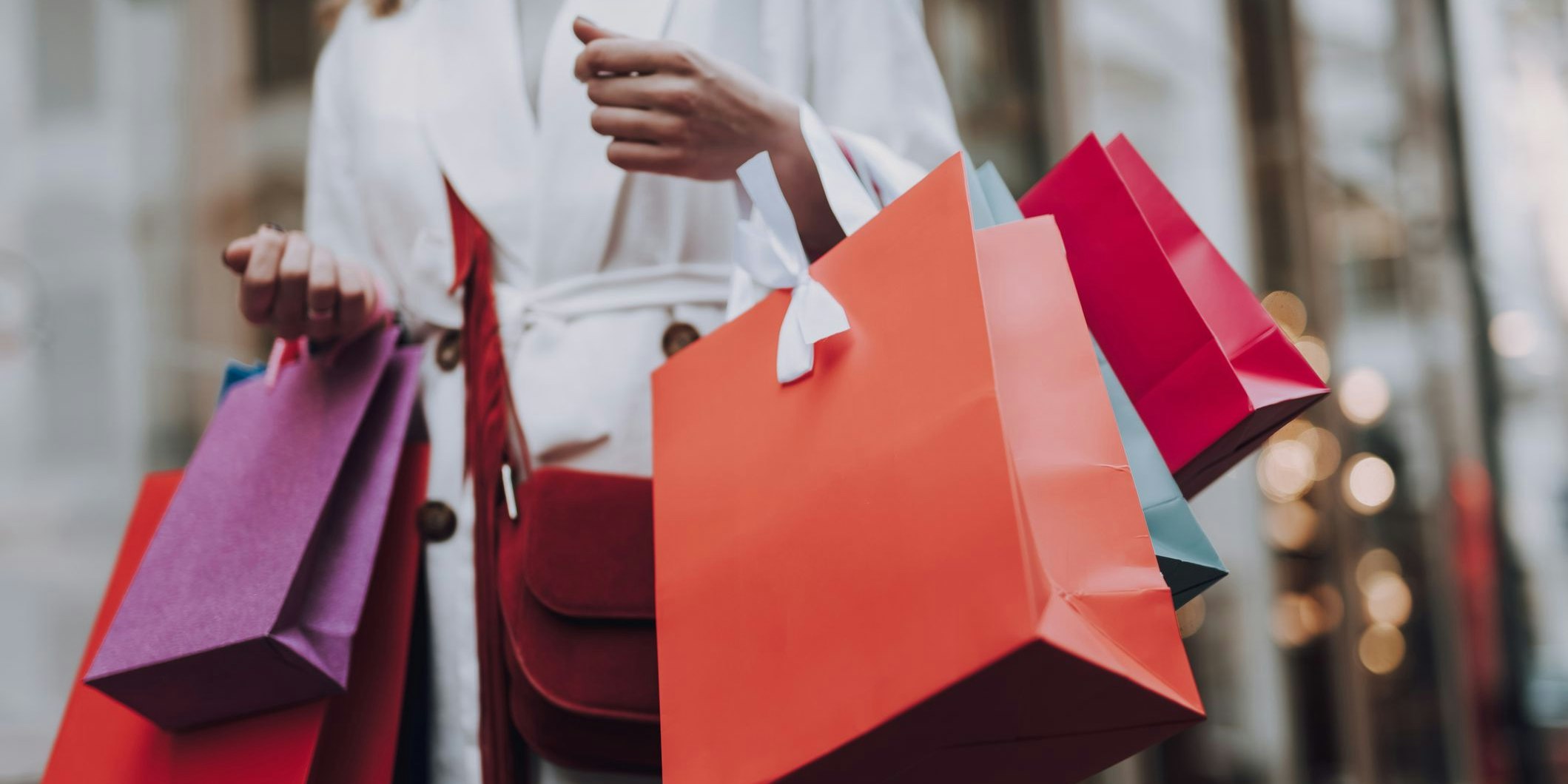 Close up of lady in white trench coat holding colorful shopping bags