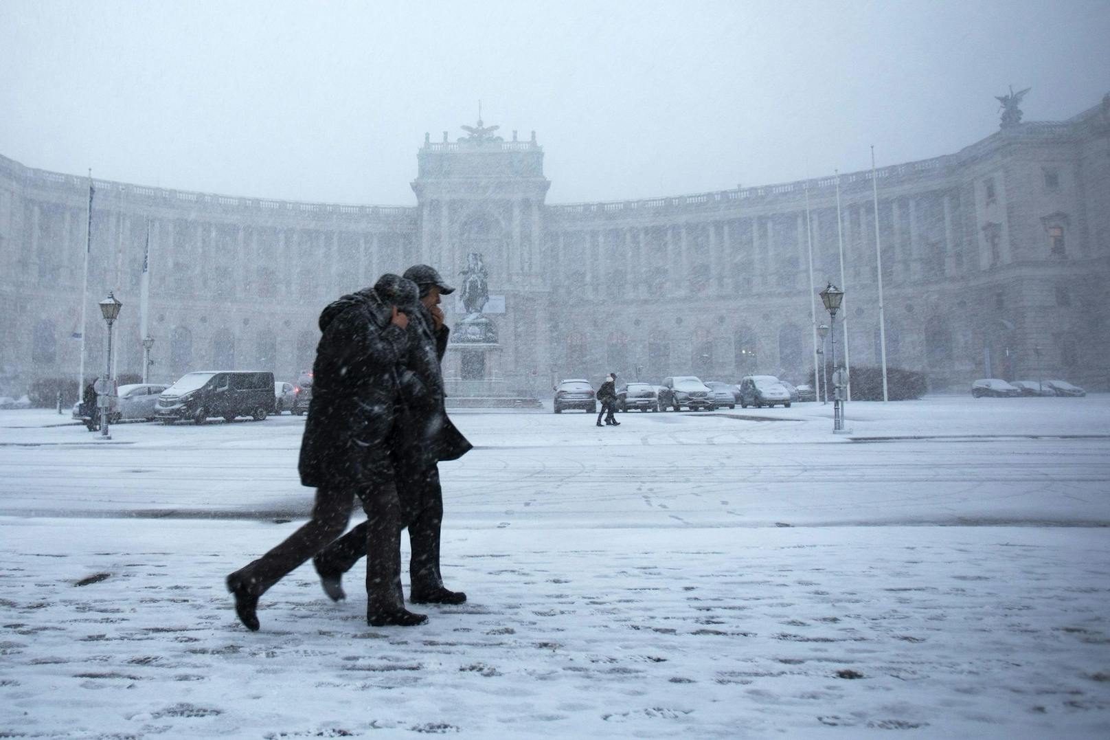 Passanten spazieren bei Schneefall über den Wiener Heldenplatz