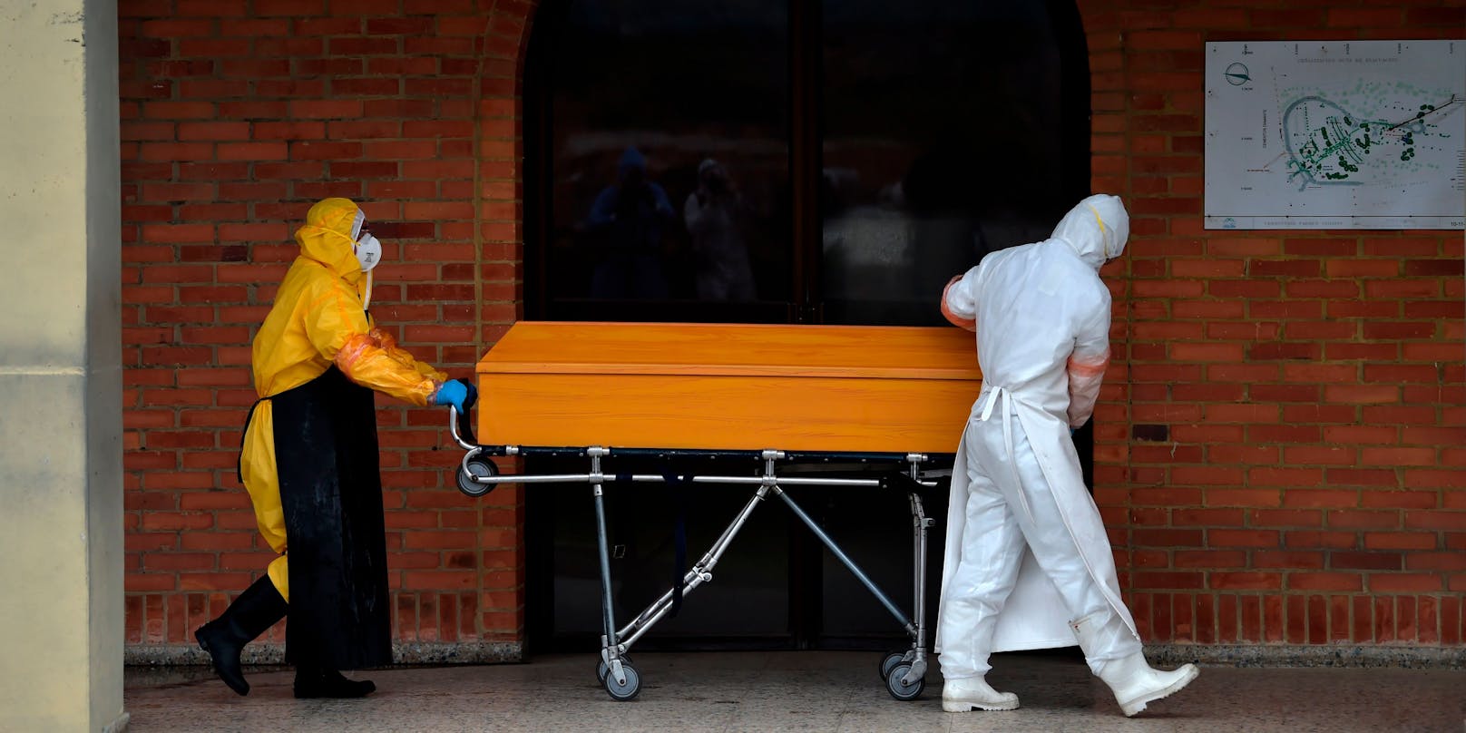 Arbeiter in Schutzkleidung transportieren einen Corona-Toten in einem Sarg. (Symbolbild)