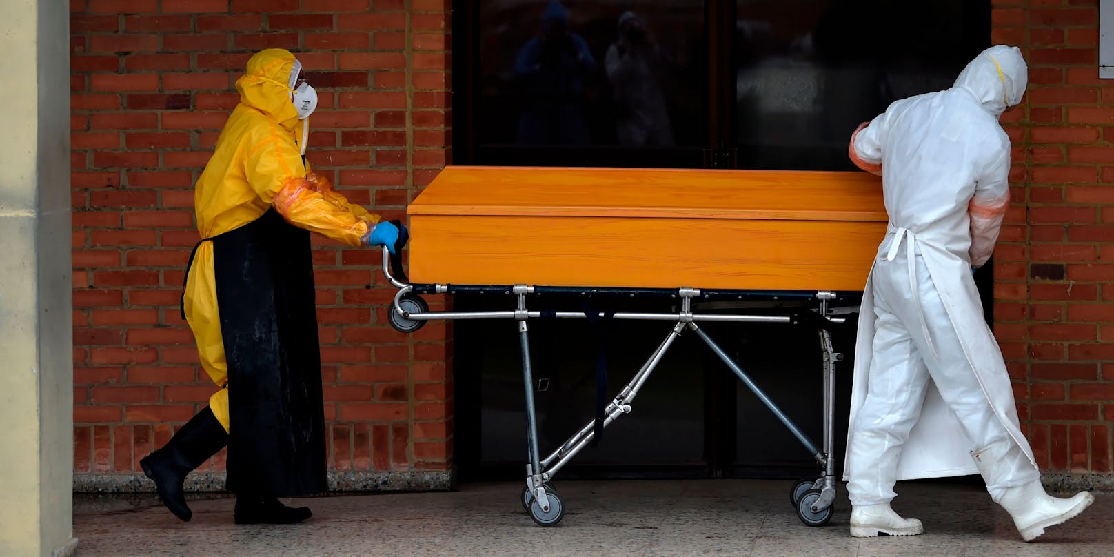 Arbeiter in Schutzkleidung transportieren einen Corona-Toten in einem Sarg. Symbolbild