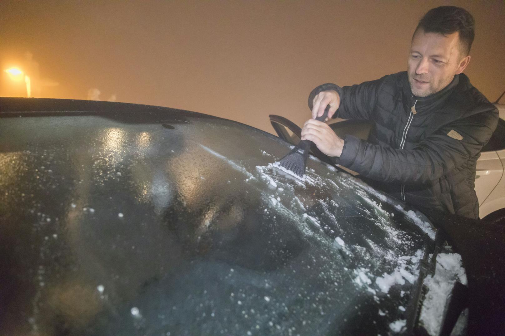 Ein Mann kratzt Eis von der Windschutzscheibe eines Autos. Symbolfoto