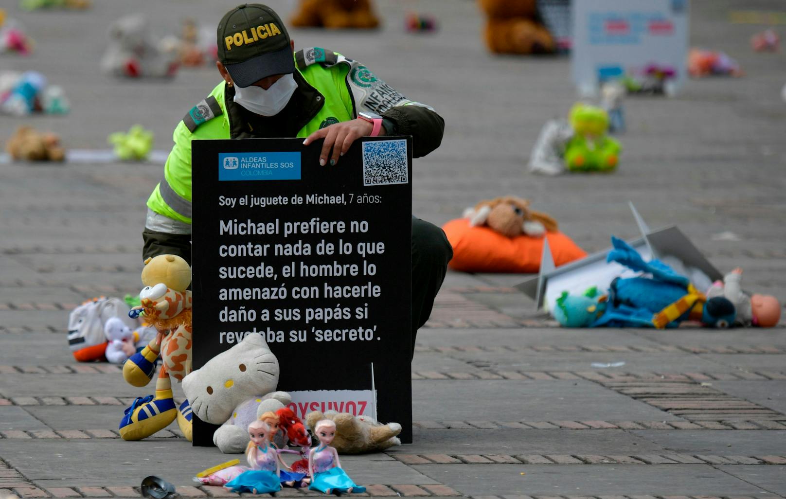 Ein Polizist platziert ein Transparent neben die Kuscheltiere. Übersetzt bedeutet dies: "Michael zieht es vor, nichts darüber zu erzählen, was mit dem Mann passiert ist, der gedroht hat seinen Eltern etwas anzutun, wenn er sein Geheimnis verraten würde."<br>