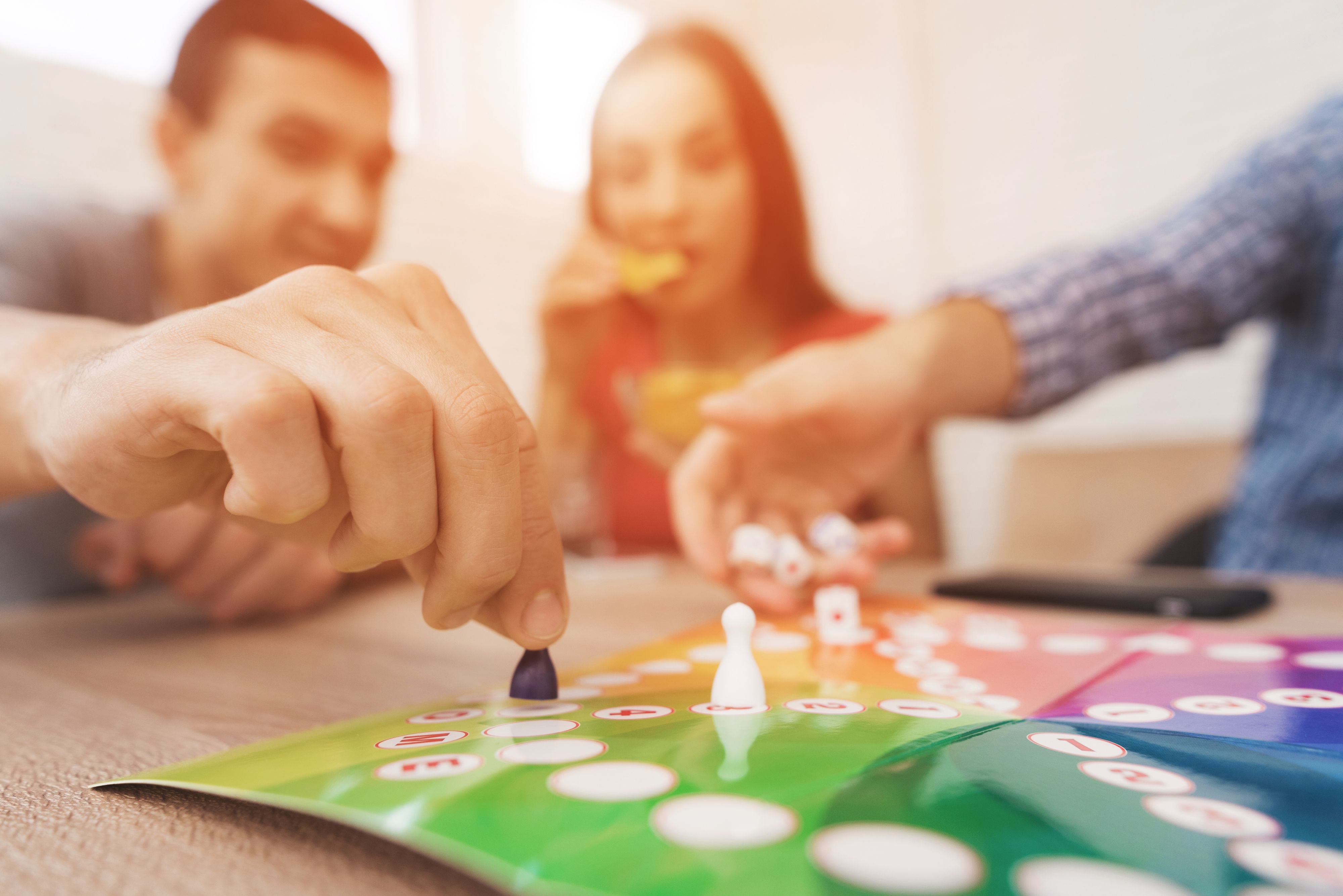 Young people play a board game using a dice and chips. On the table they have glasses with alcoholic drinks. They have fun playing a game.