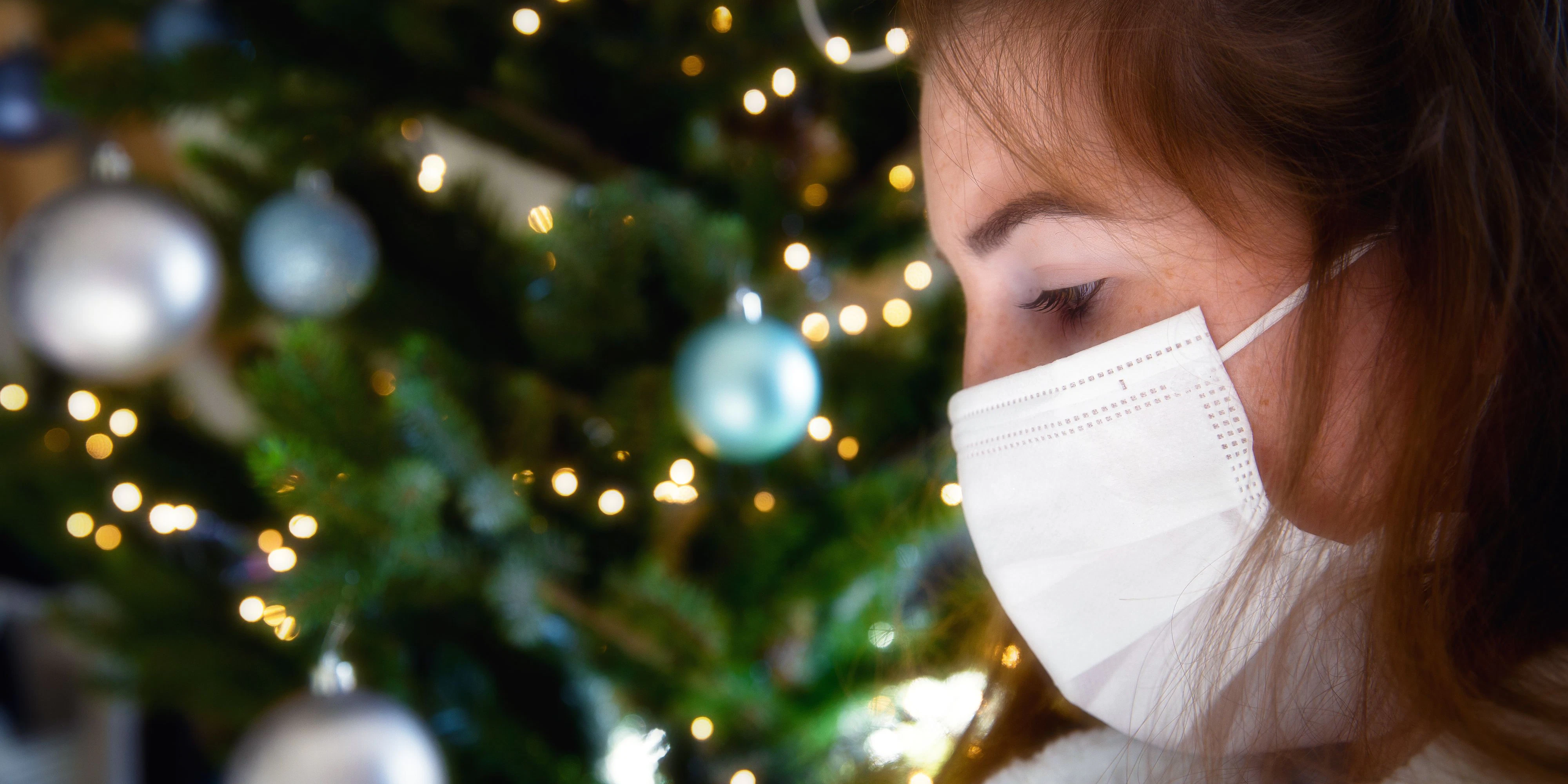 Porträt einer jungen Frau mit schützender Gesichtsmaske vor einem Christbaum