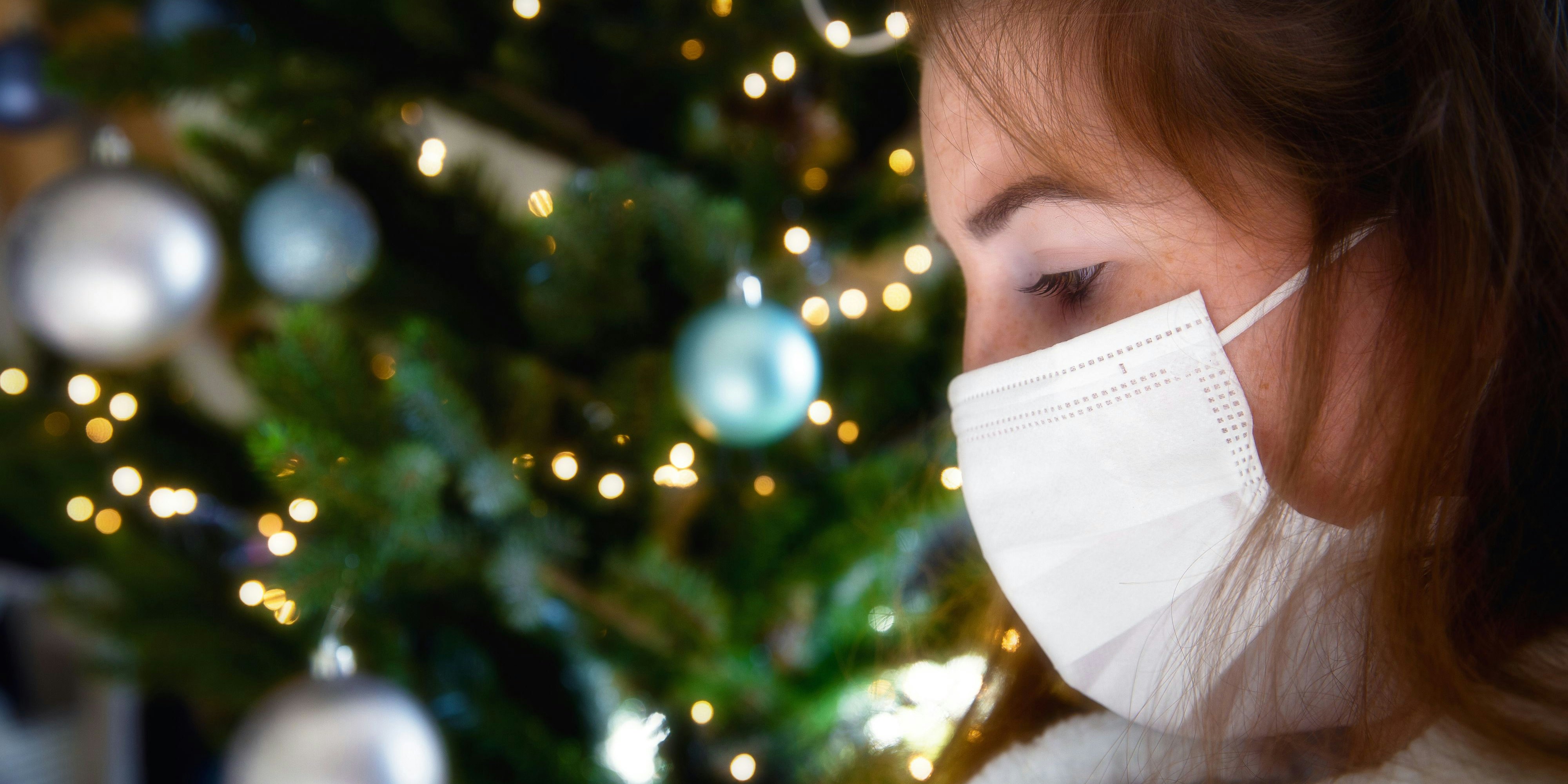 Porträt einer jungen Frau mit schützender Gesichtsmaske vor einem Christbaum