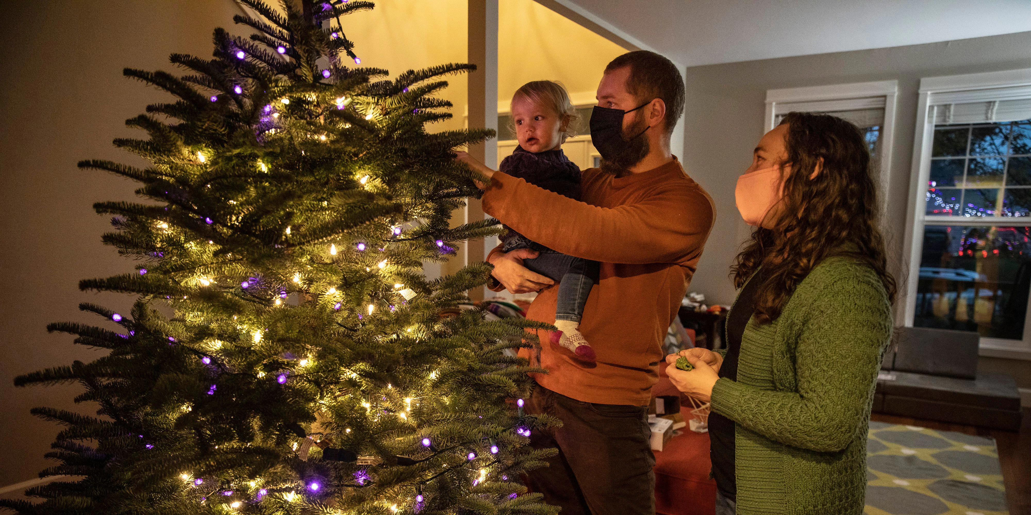 Download von www.picturedesk.com am 17.12.2020 (11:38).  Ani Sirois places lights and decorations on the family's Christmas tree with daughter Ida, 2, and husband, Chadwick, at their home on Tuesday, Nov. 24, 2020 in Portland, Ore. Sirois, a respiratory nurse, has spent months caring for coronavirus patients at a Portland hospital. But on a recent sunny day, COVID-19 seemed far away as she, her husband and their 2-year-old daughter roamed a Christmas tree farm in search of the perfect evergreen for a holiday season unlike any other. The family was tree-shopping nearly a week before Thanksgiving and, for the first time, they were picking their own tree instead of buying a pre-cut one. (AP Photo/Paula Bronstein) - 20201123_PD8184 - Rechteinfo: Rights Managed (RM)