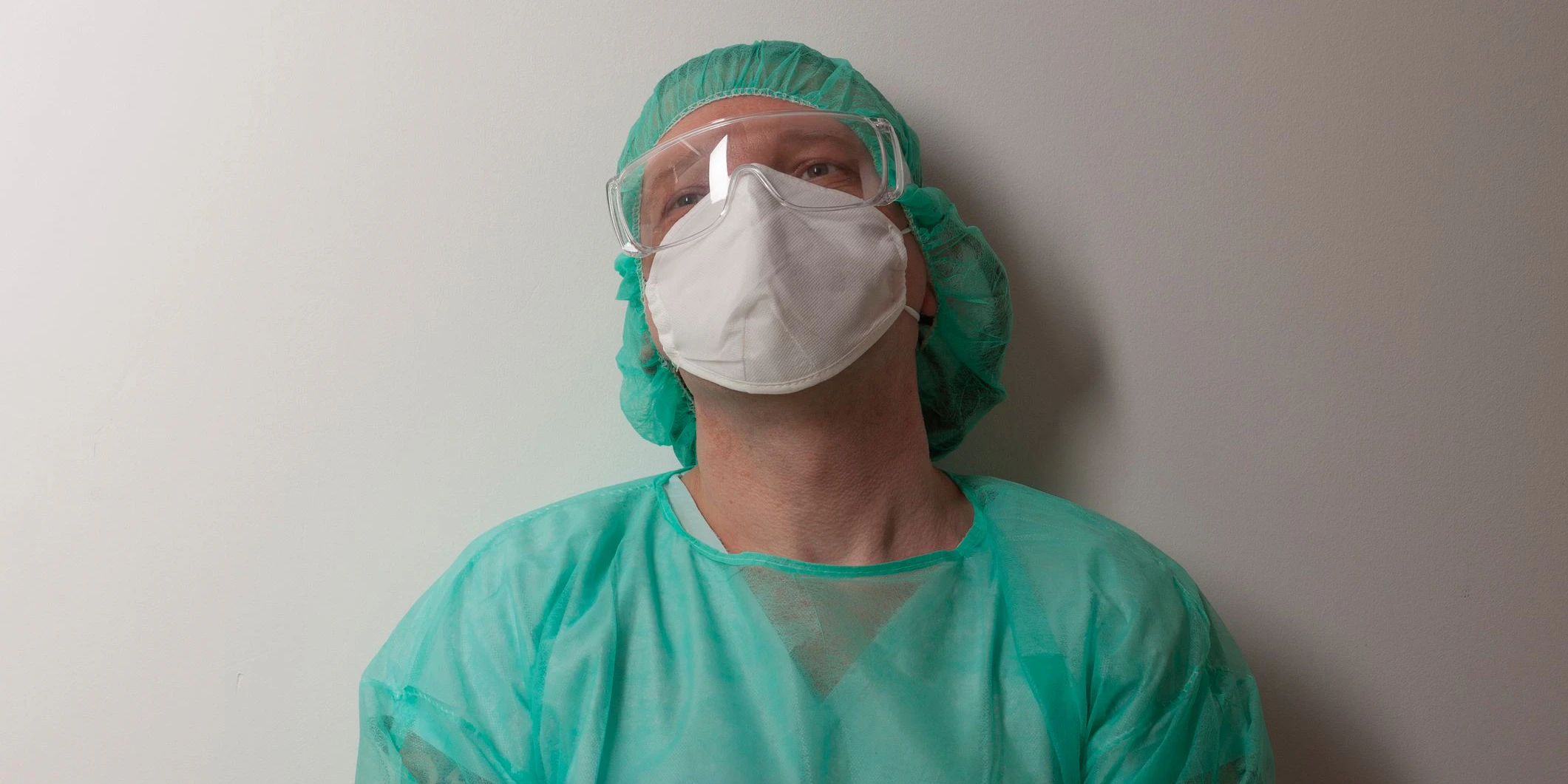 Tired male nurse, with plastic protective eyeglasses and respirator ffp2, cap, gown, with  personal protective equipment to protect against the virus covid-19 in ICU in hospital.