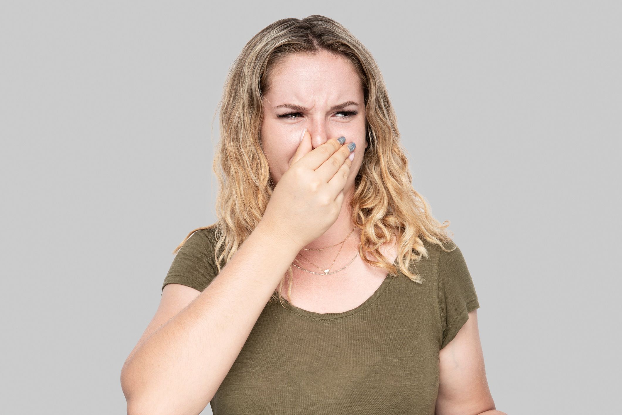 Girl covers nose with hand showing that something stinks isolated on gray background.