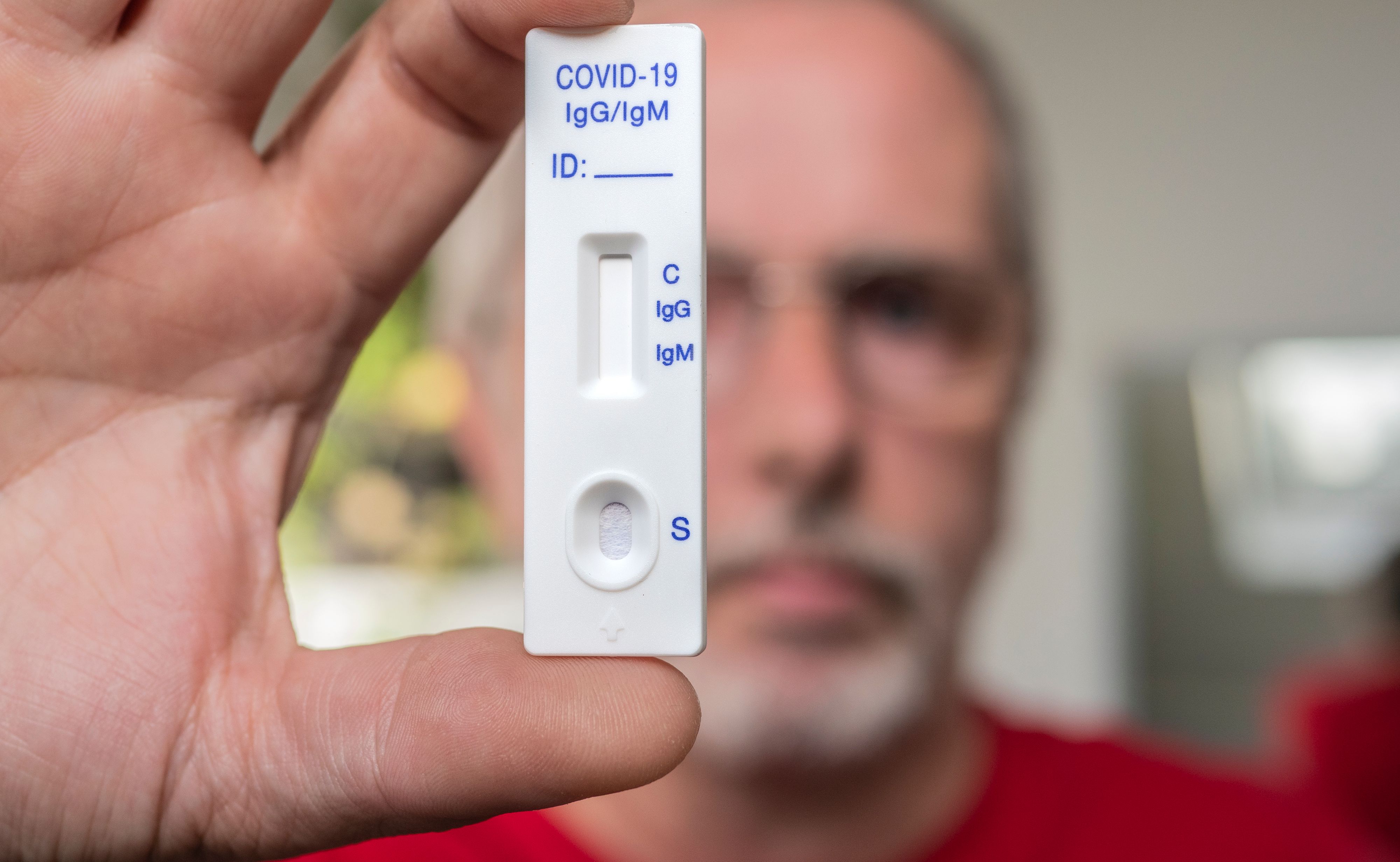 A man wearing glasses holding Covid-19 immunity test in front of him