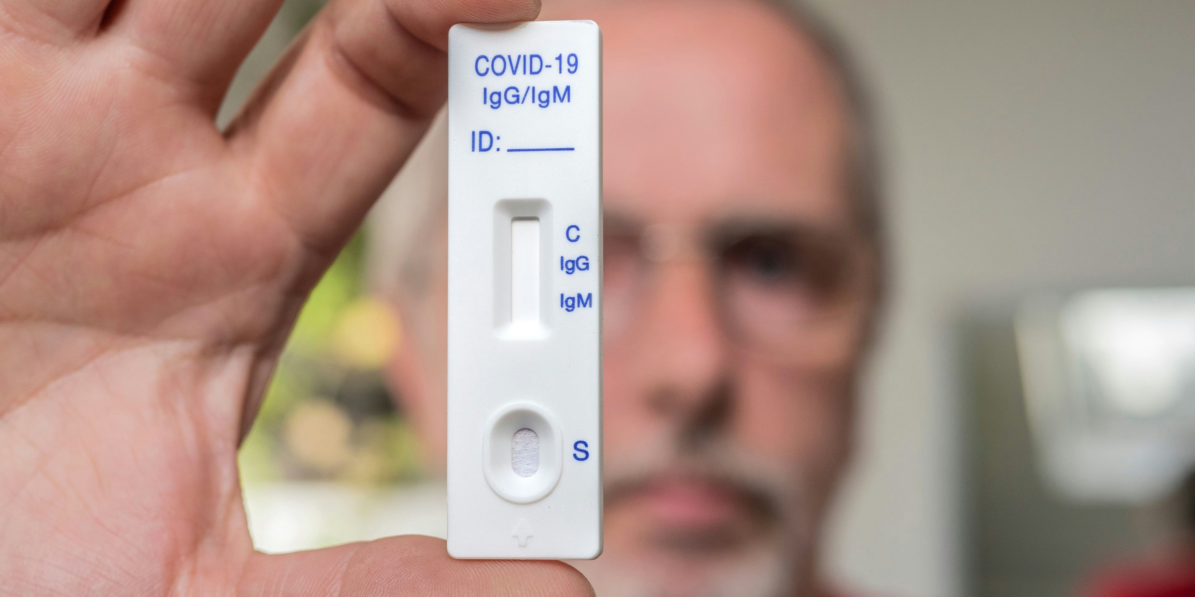 A man wearing glasses holding Covid-19 immunity test in front of him