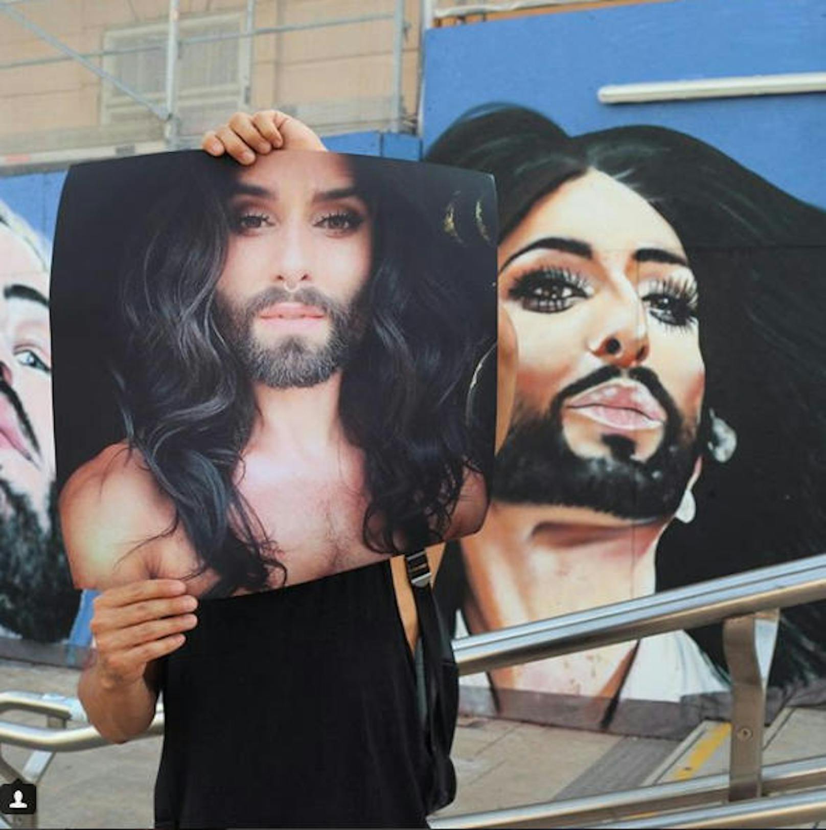 03.08.2017: Conchita Wurst posiert mit einem Foto vor ihr Gesicht gehalten vor einem Wandgemälde beim Museumsquartier in Wien. Sie bittet den Künstler, das nächste Mal bitte auf das von ihr gezeigte Portrait zurückzugreifen.