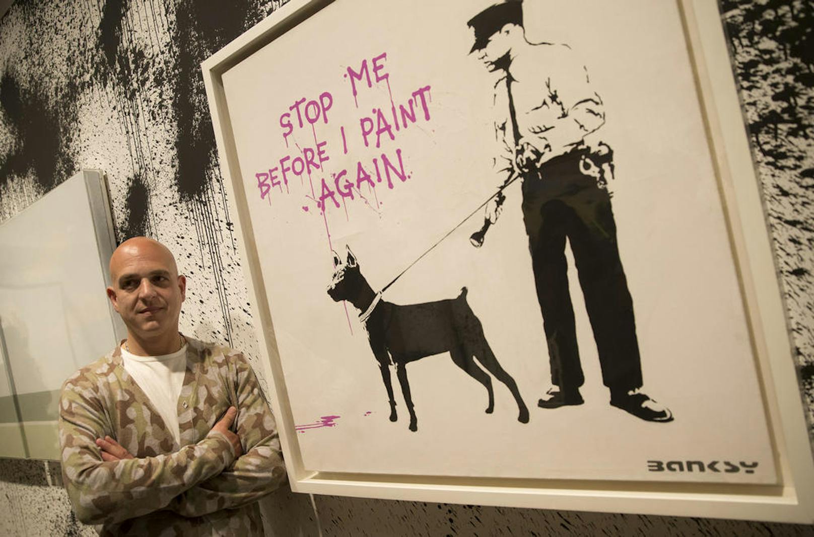 Dieser Mann im Bild ist NICHT Banksy, sondern posiert nur neben einem Werk des Künstler-Phantoms.