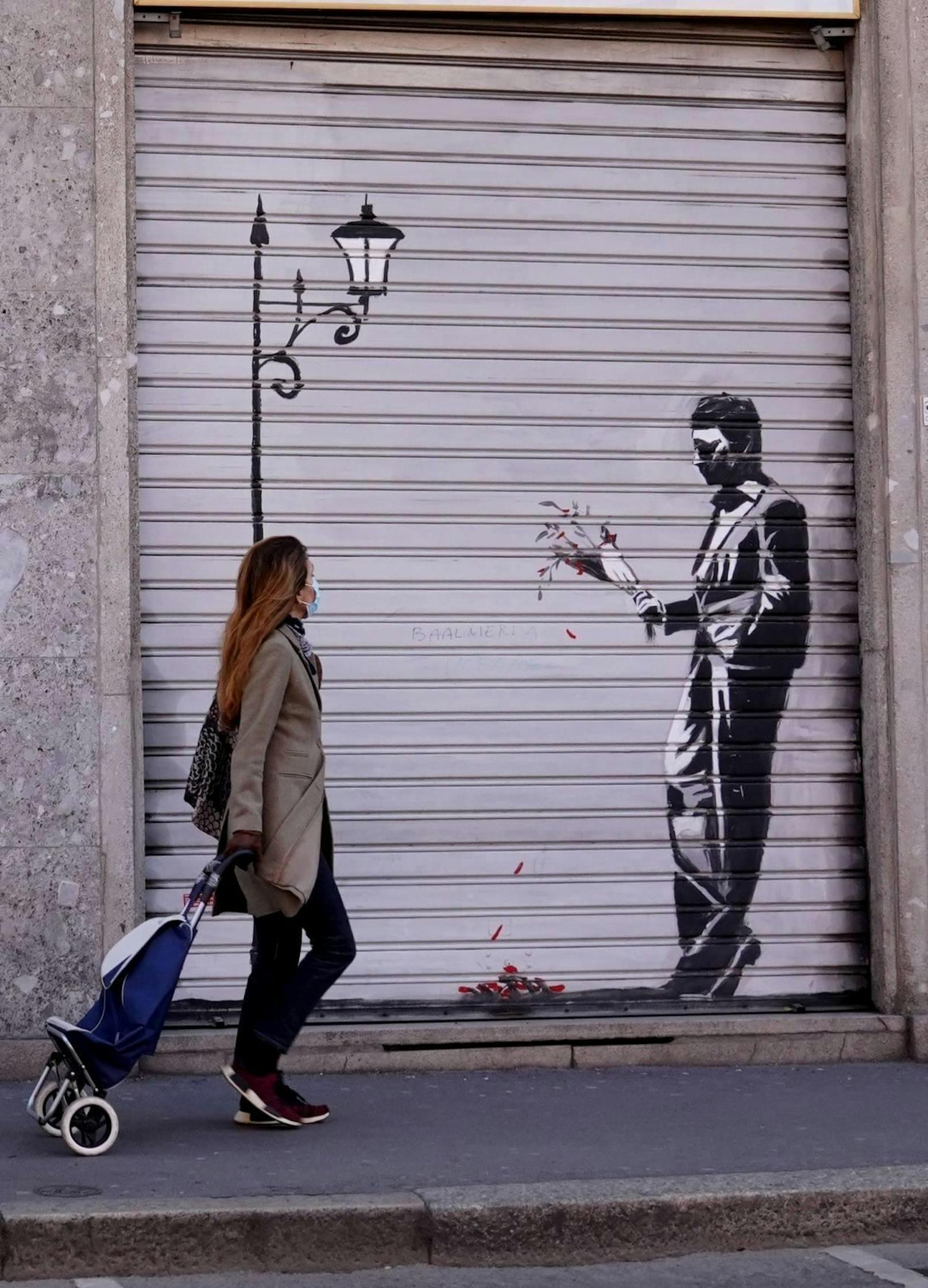 Anfang April 2020 in Mailand: Mitten in der Coronakrise geht eine Frau mit Maske an einem Banksy-Gruß vorbei
