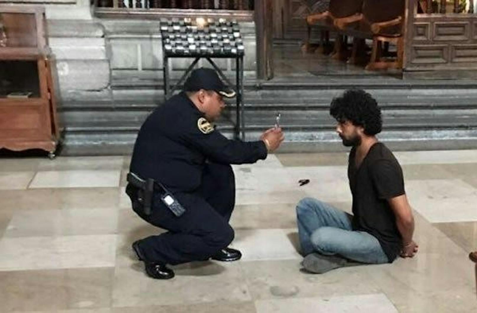 Gefasst! Der Täter sitzt mit Handschellen gefesselt auf dem Boden der Kirche - ein Polizist fotografiert ihn.
