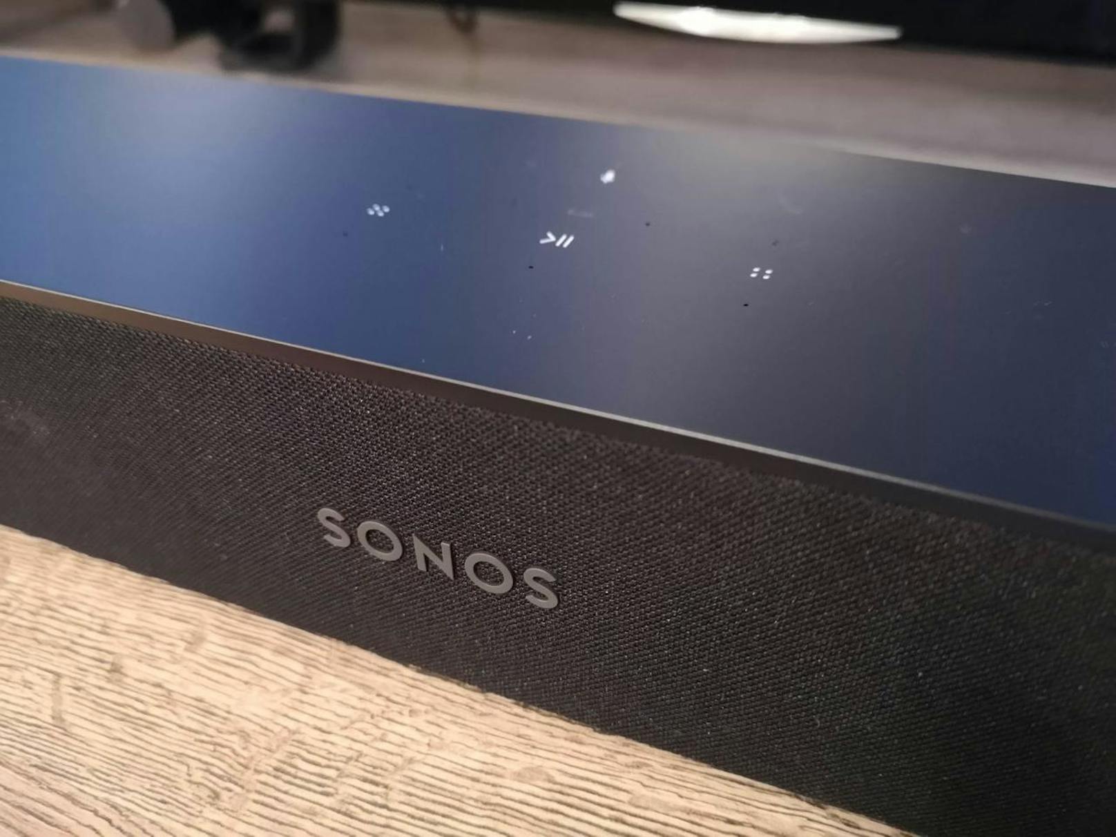 Auf der Vorderseite prangt das Sonos-Logo, auf der Oberseite finden sich die Touch-Buttons für Lautstärke, Musikauswahl und Mikrofon-Stummschaltung. Eine kleine LED zeigt an, ob die Soundbar zuhört, ob sie stumm geschalten ist oder ob sie gerade Feedback gibt.
