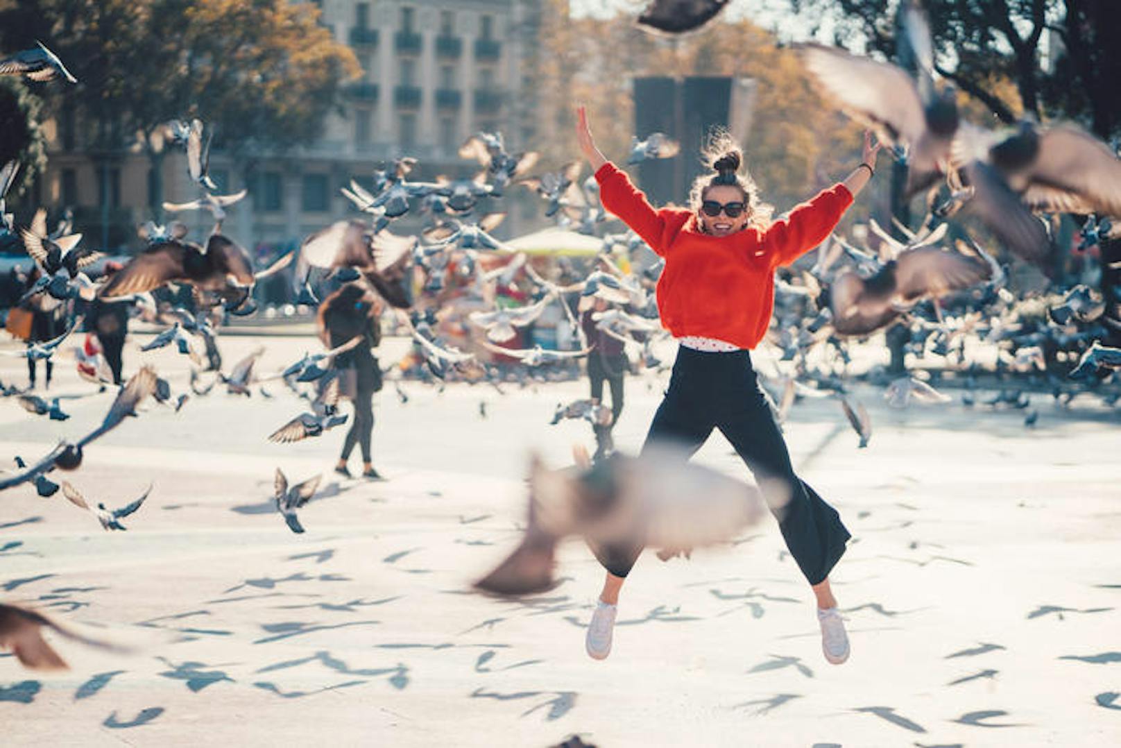 Young girl at Placa de Catalunya jumping happily among the pigeons