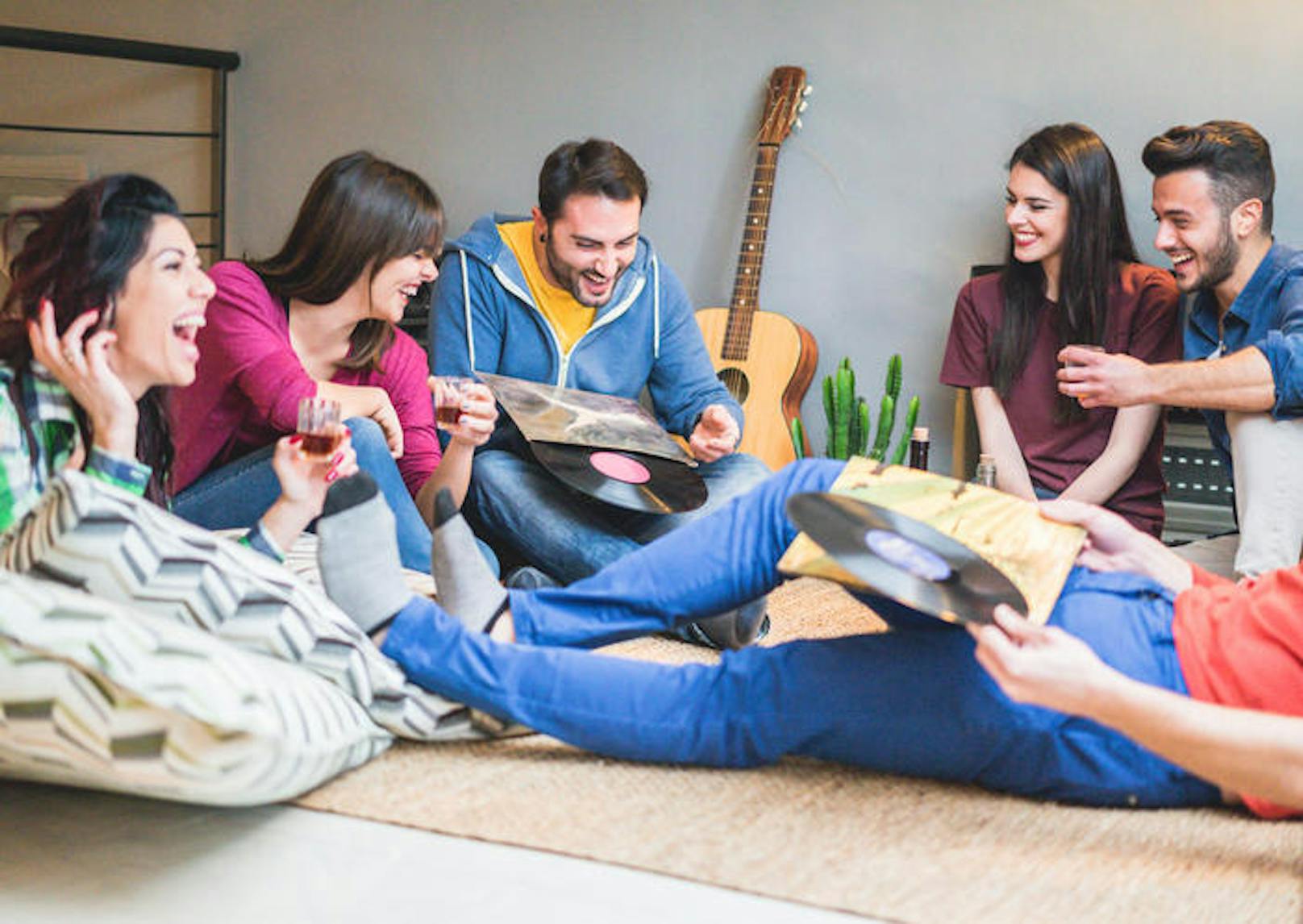 Happy friends having party listening vintage vinyl disc albums in hostel room - Young people having fun drinking shots and laughing together - Soft focus on left man face - Warm filter (Happy friends having party listening vintage vinyl disc albums in