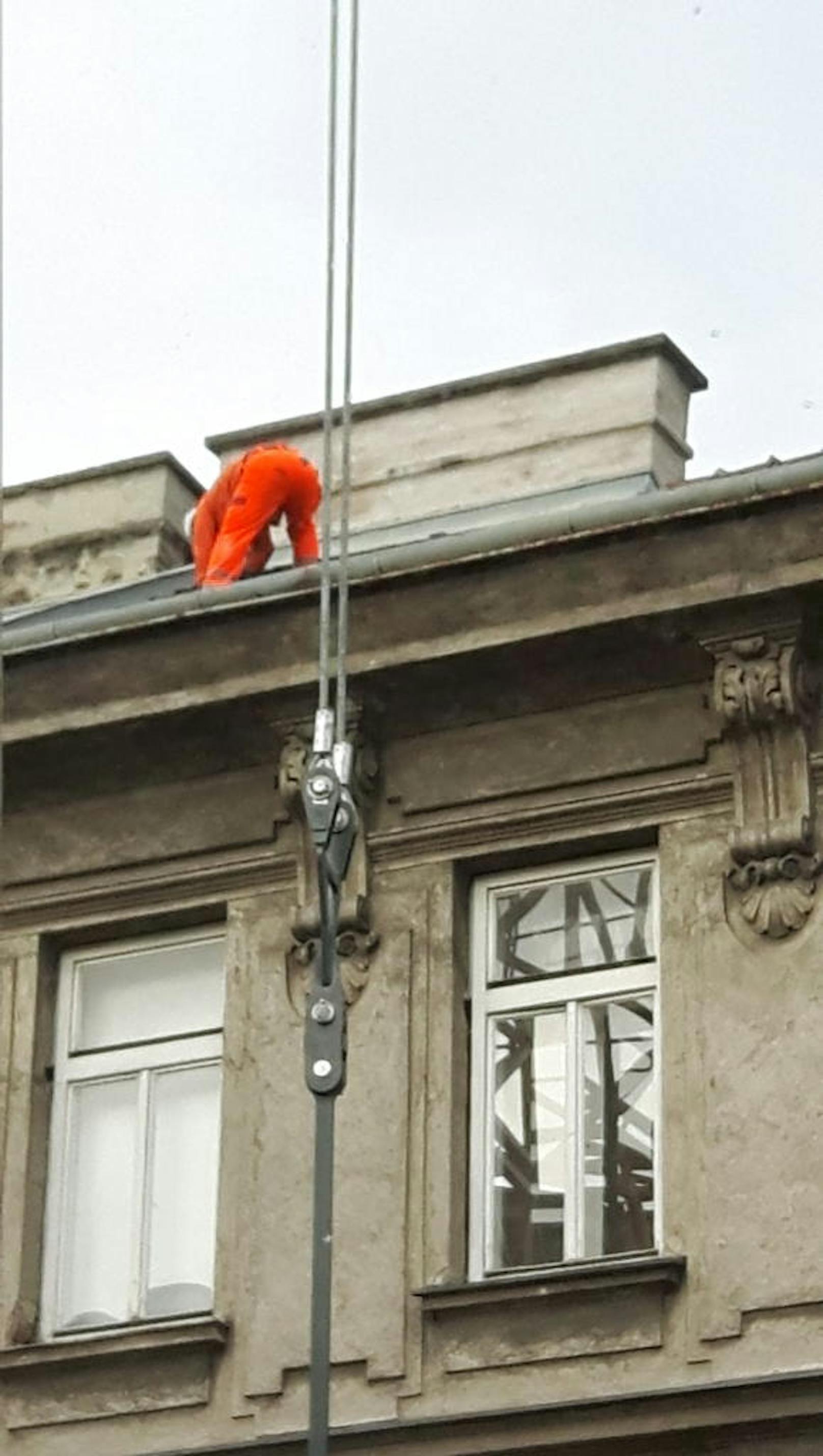 Vollkommen ungesichert arbeitet der Mann in Orange in schwindelerregender Höhe auf dem Dach eines Wiener Wohnhauses.