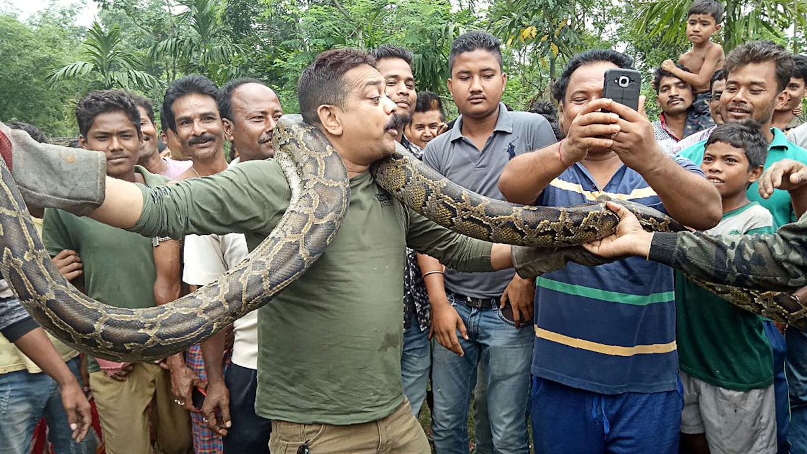 Während Förster Sanjay Dutta (Mitte) aus Westbengalen für Fotos vor einer jubelnden Menge mit einer fünfeinhalb Meter langen Python posierte, wurde er von dieser beinahe erdrosselt (17. Juni 2018).