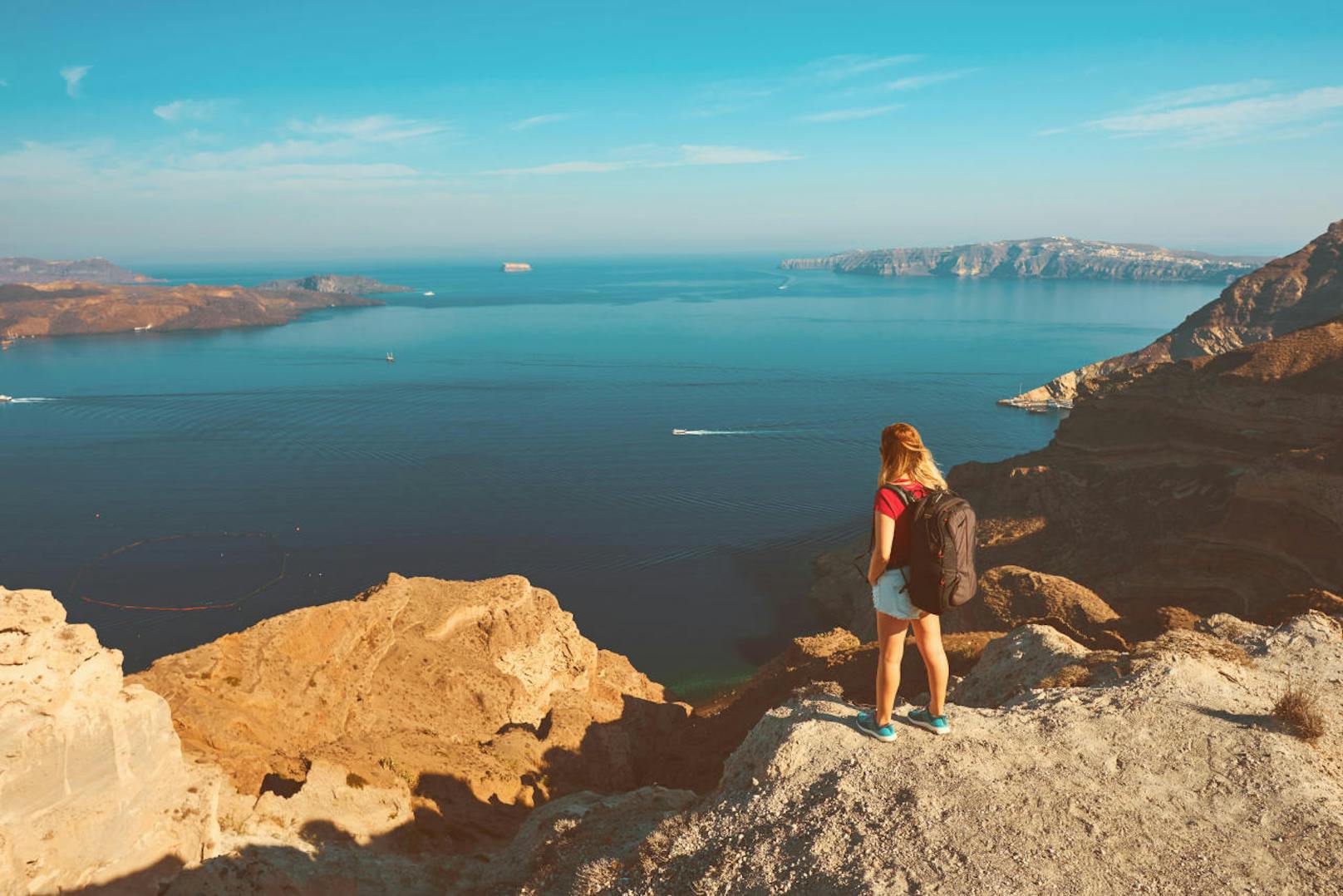hiker woman carrying her backpacker, enjoying the summer view from Santorini island.