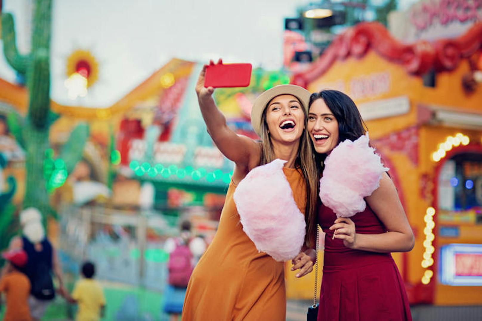 Happy girlfriends are taking selfie/making video call and make fun together in fun fair