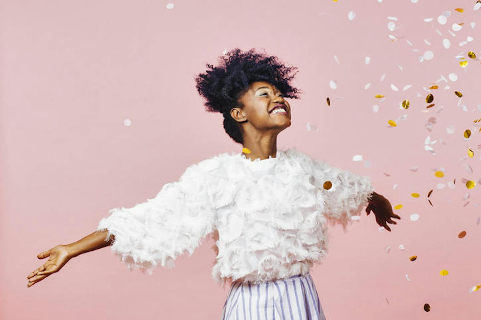 Portrait of a young girl with a big smile throwing confetti in the air, isolated on pink studio background