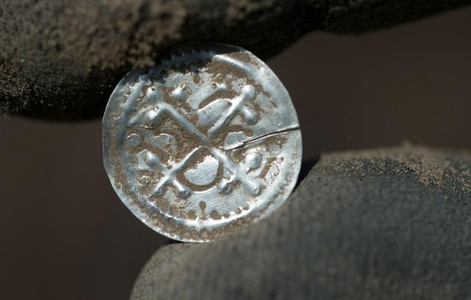 Ein Kreuzbrakteate unter Harald Blauzahn (936-984); erster eigenständiger Münztyp Dänbemarks hält eine Archäologe nach der Ausgrabung. Mit einem Silbergewicht von 0,3 Gramm hatten die mit einem christlichen Kreuz versehenen Brakteate nur einen geringen Silberwert.
