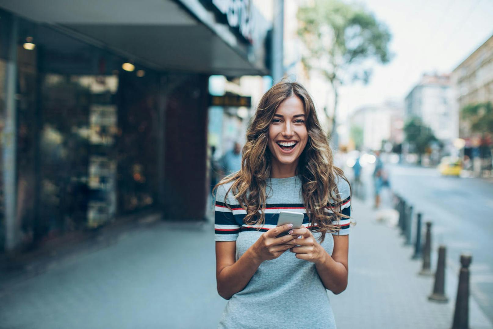 Young woman with smart phone walking on the street and laughing, with copy space.