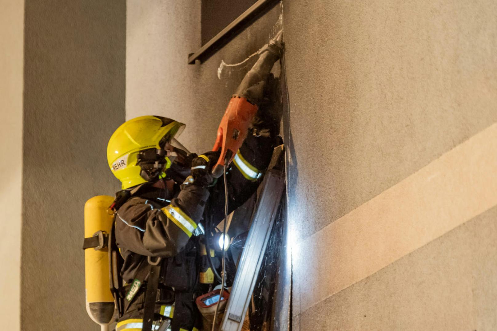 Ein Feuerwehrmann öffnet mit schwerem Gerät die Fassade.