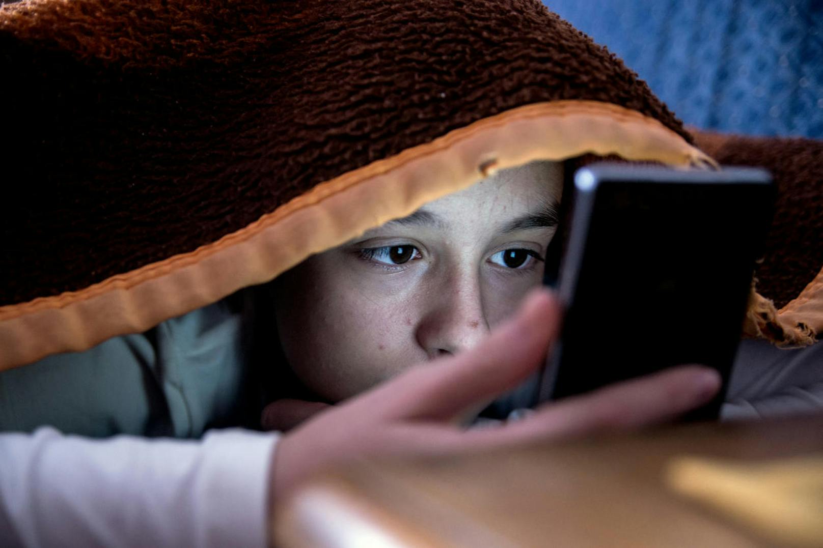 Kann den Schlaf nachhaltig stören: Ein Kind spielt im Bett mit seinem Smartphone.