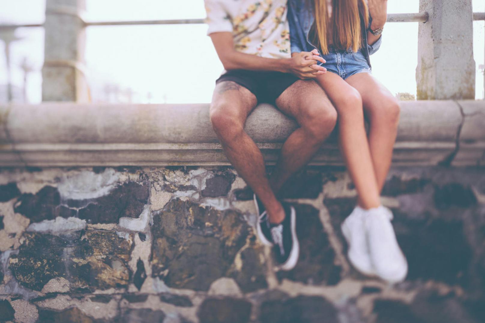 Cropped image of the legs of a hipster couple holding hands and sitting on a wall made of rough textured stone (Cropped image of the legs of a hipster couple holding hands and sitting on a wall made of rough textured stone, ASCII, 110 components, 110 