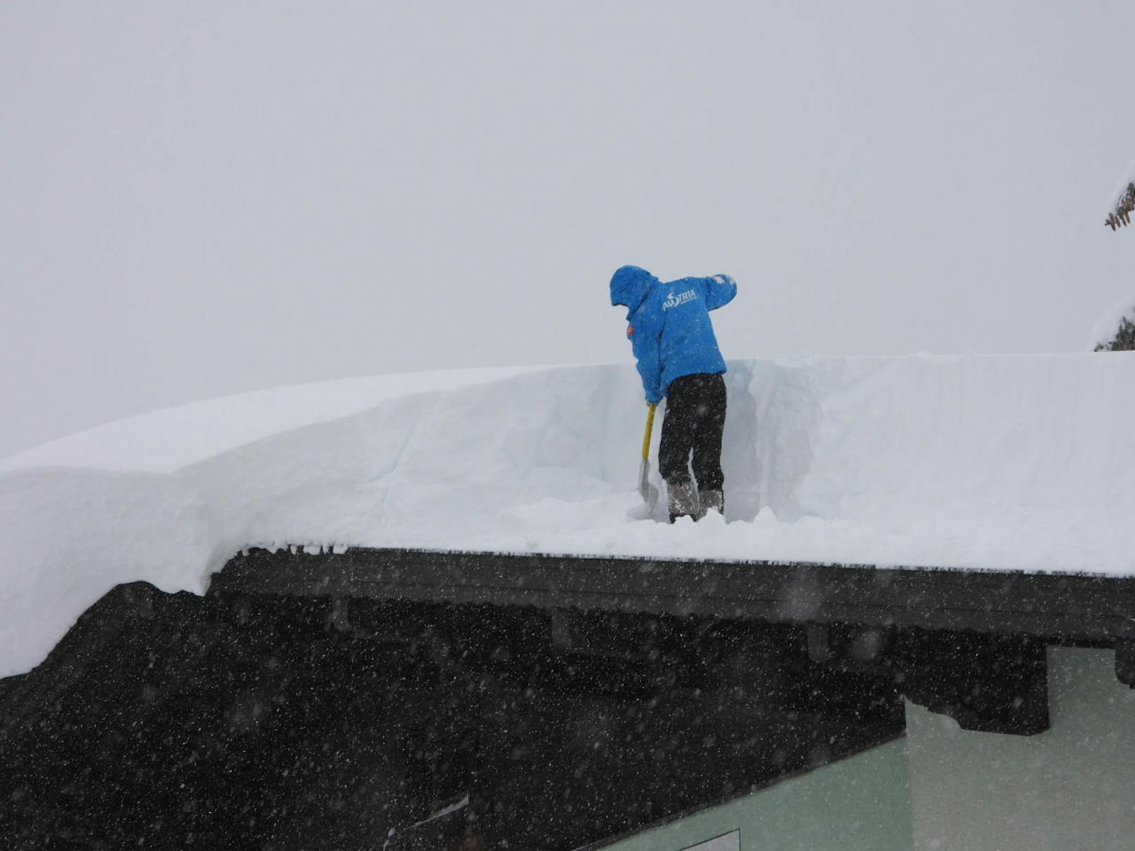 Ein Mann bei der Schneeräumung am Dach eines Hauses in Hochfilzen.