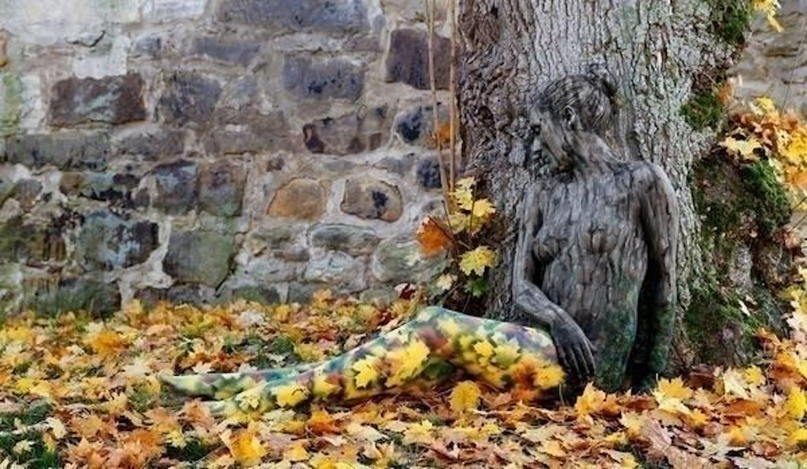 Die Frau scheint am Fuße des Baumes zu schlafen. Augenscheinlich will sie nicht gestört werden, denn sie hat sich mit den Farben der Natur getarnt.
