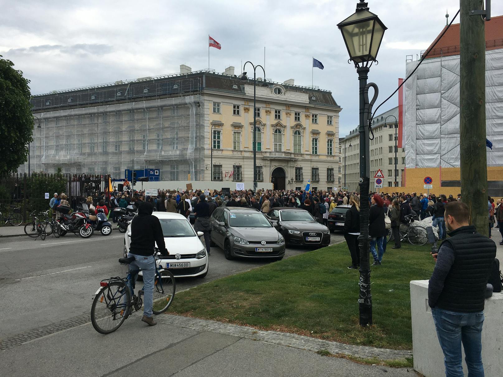 Mit Schildern, Parolen und reichlich Abstand tummeln sich Dutzende Menschen vor dem Bundeskanzleramt.