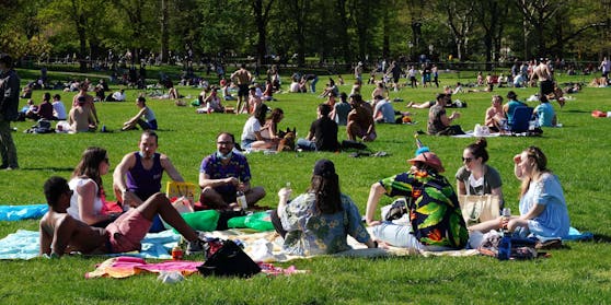 Zahlreiche Menschen genießen die Sonne in einem Park.