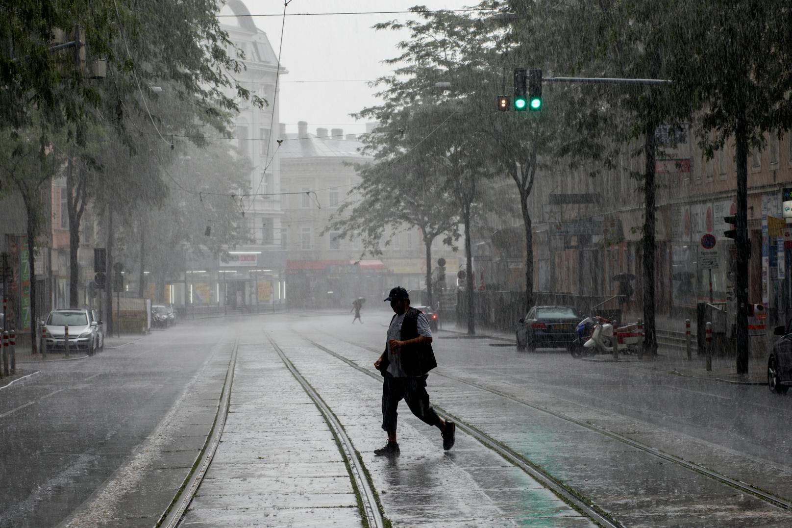 Ein Mann geht während eines starken Regens über die Straßenbahn-Gleise in der Mariahilferstraße.