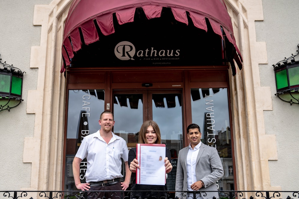 Bei ihrer neuen Lehrstelle: Samantha T. mit Rathaus-Café-Besitzer Martina Schödl und Gewerkschafter Sumit Kumar
