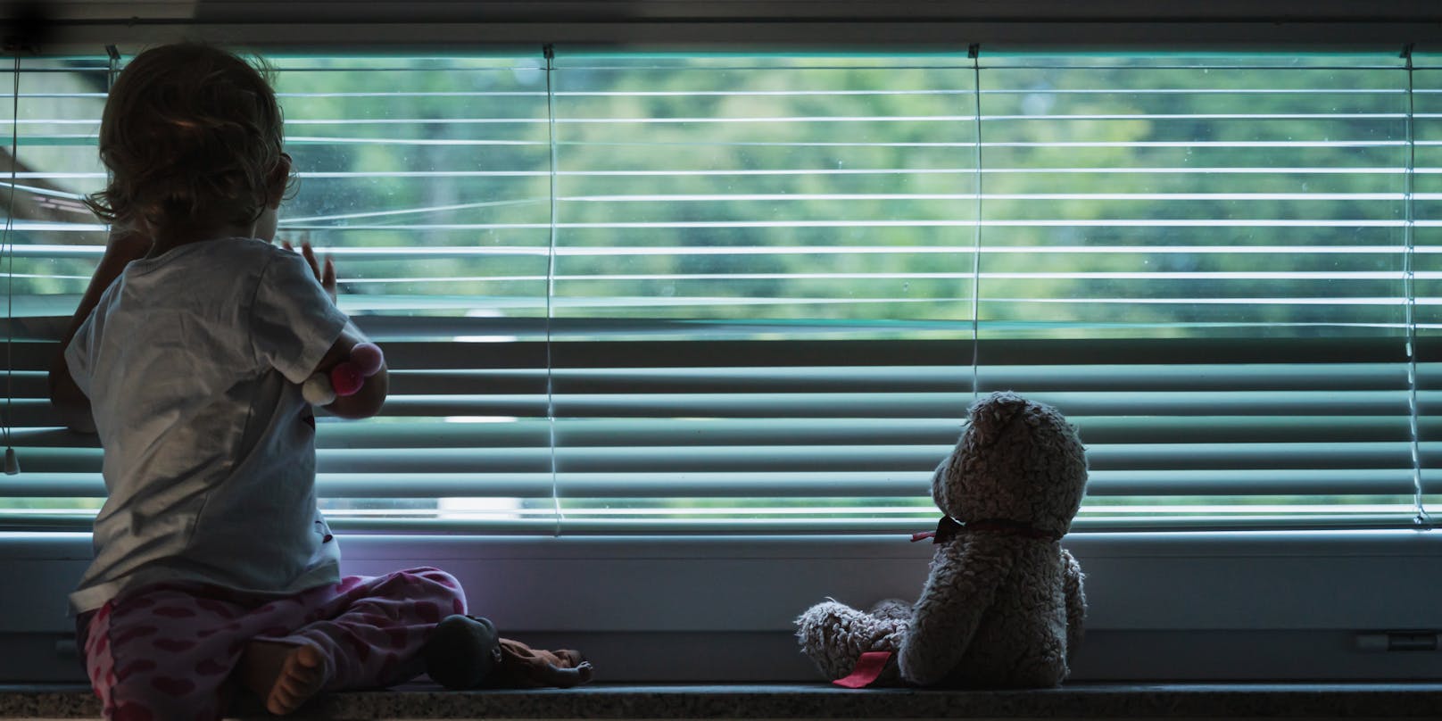 Ein kleines Mädchen schaut traurig aus dem Fenster. Symbolbild