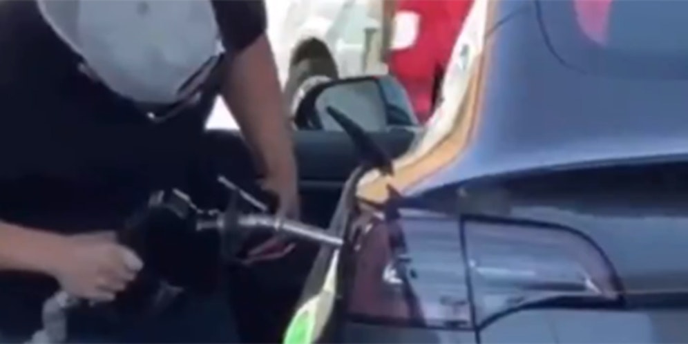 Verzweifelt sucht der junge Mann nach dem Tankstutzen des Tesla.