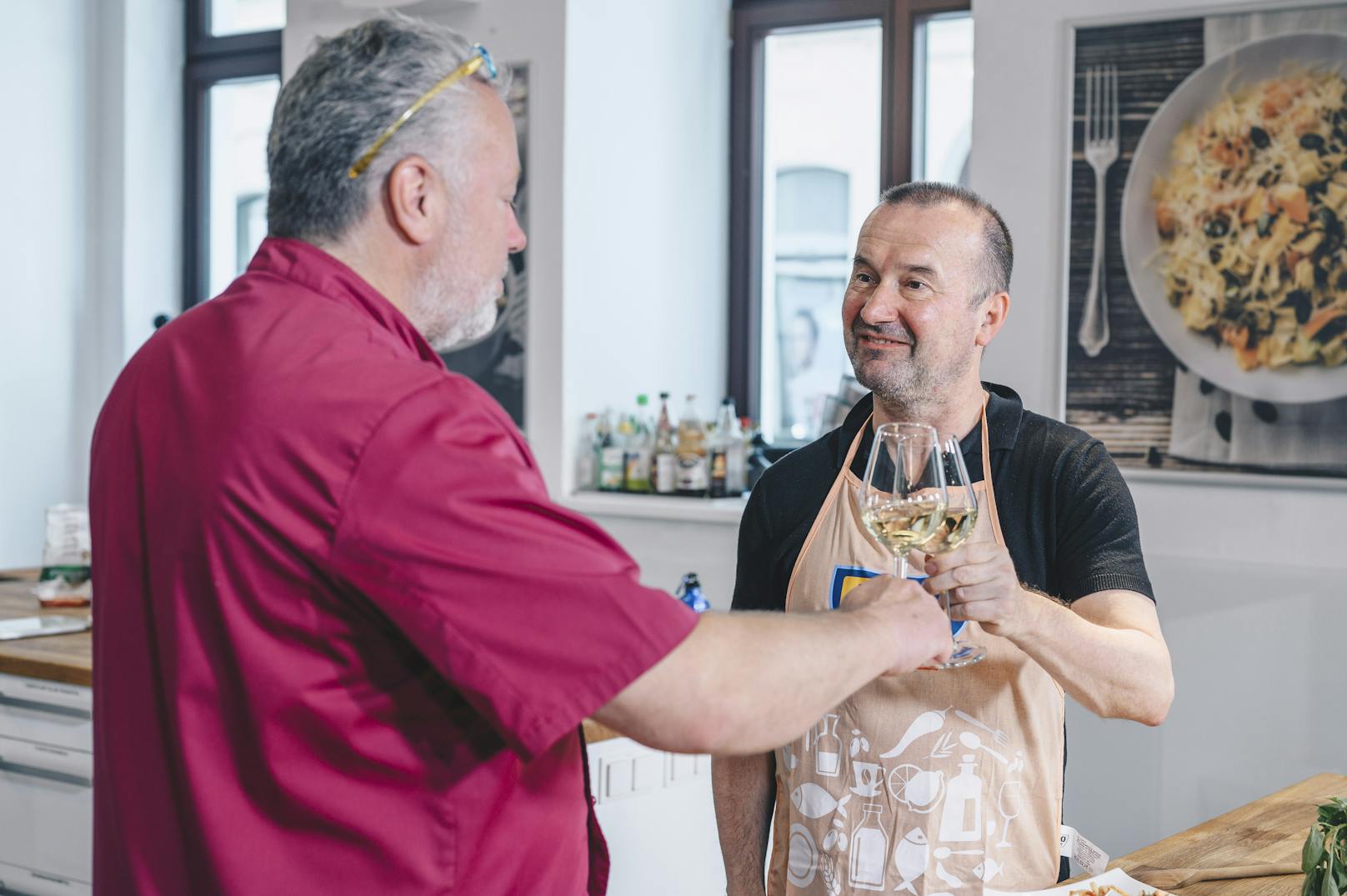 Gewinner Konrad und Profi-Koch Erik Pauer stoßen mit einem Glas Weißwein auf die gemeinsame Kochstunde an.
