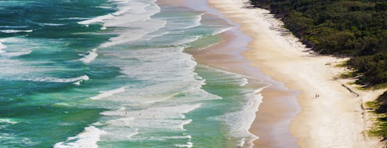 Surfer auf dem Weg ins Wasser am Tallow Beach in Australien.