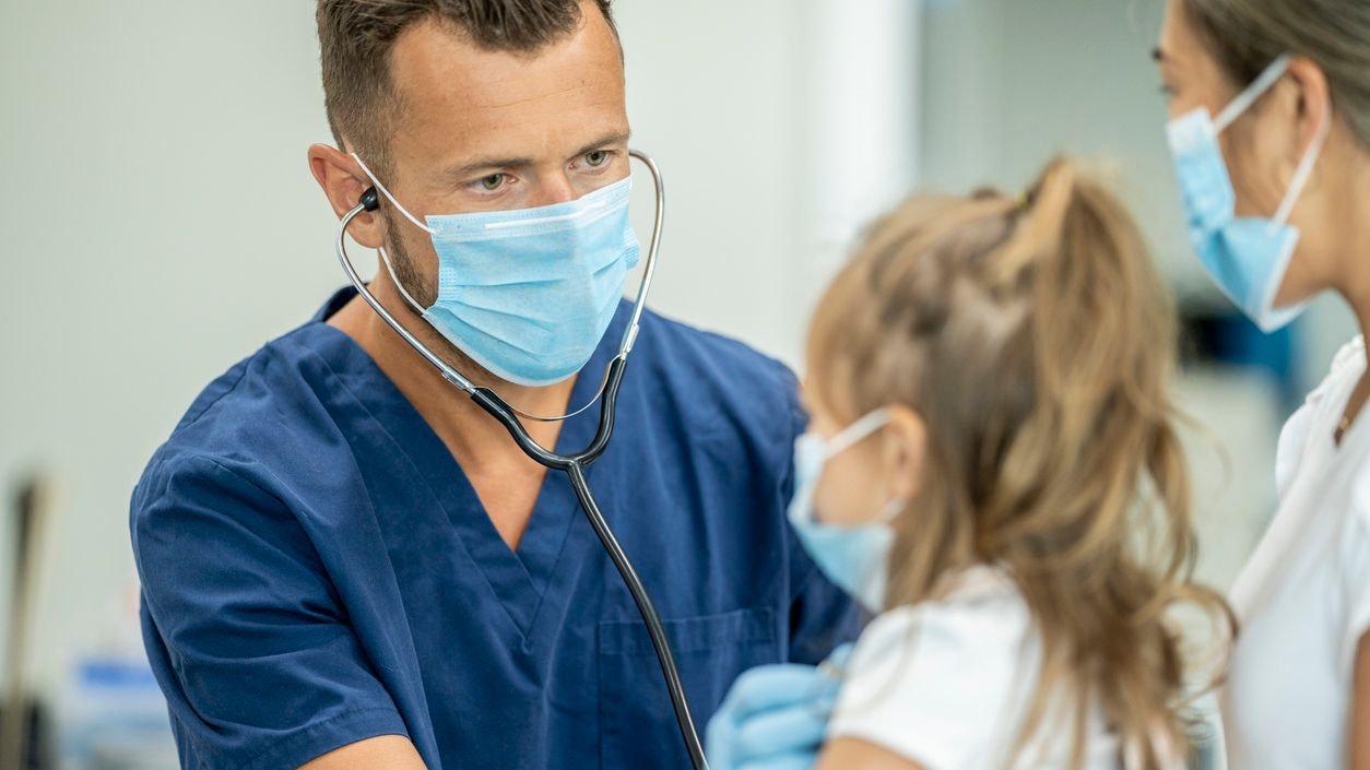 Mother and daughter visit the doctors office wearing protective face masks for the checkup to avoid the transfer of germs during COVID-19.